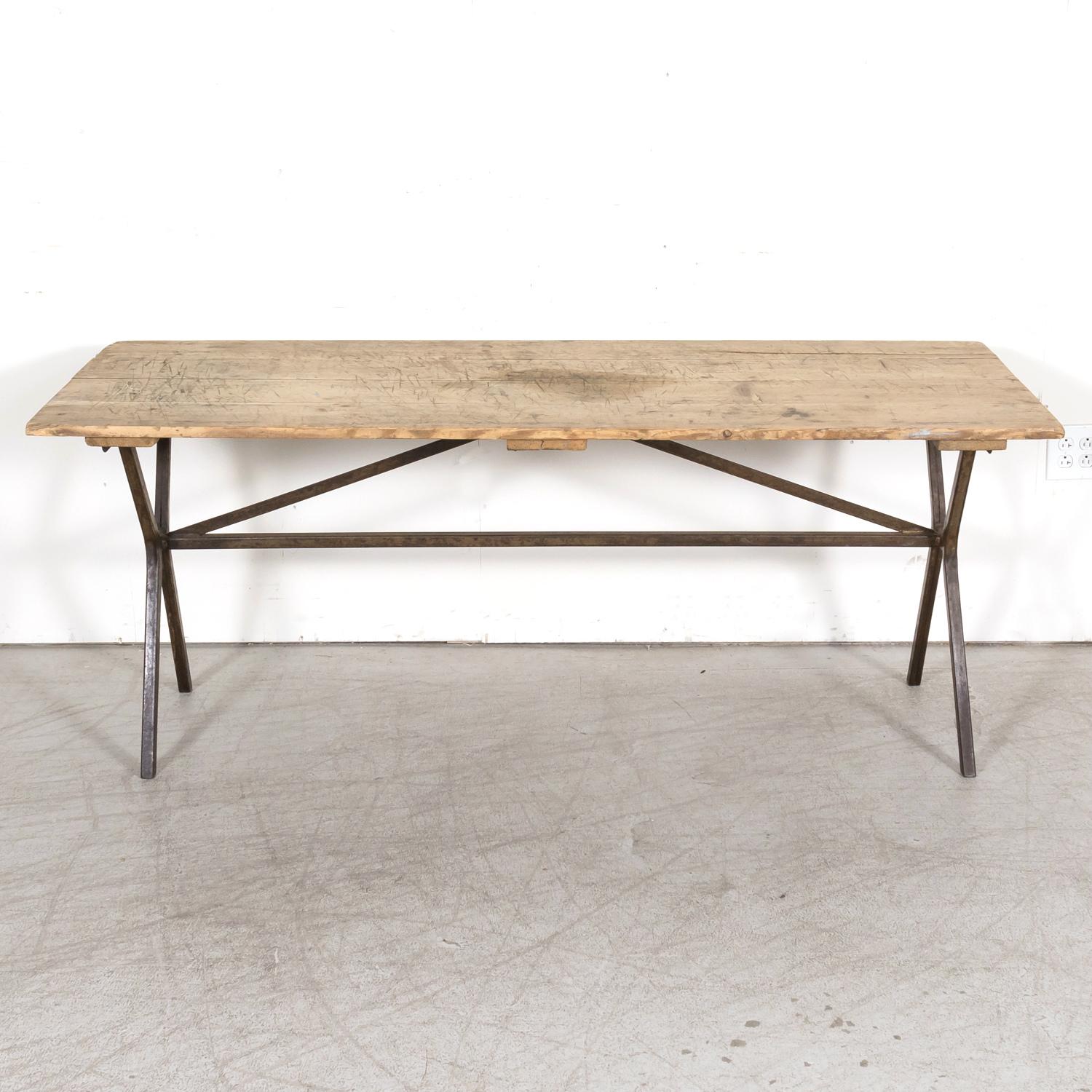 Early 20th century French bistro or pub table from Toulouse, having a typical rustic washed oak removable plank top and iron trestle base joined by iron stretchers that provide additional stability. This table would be perfect as a console table or