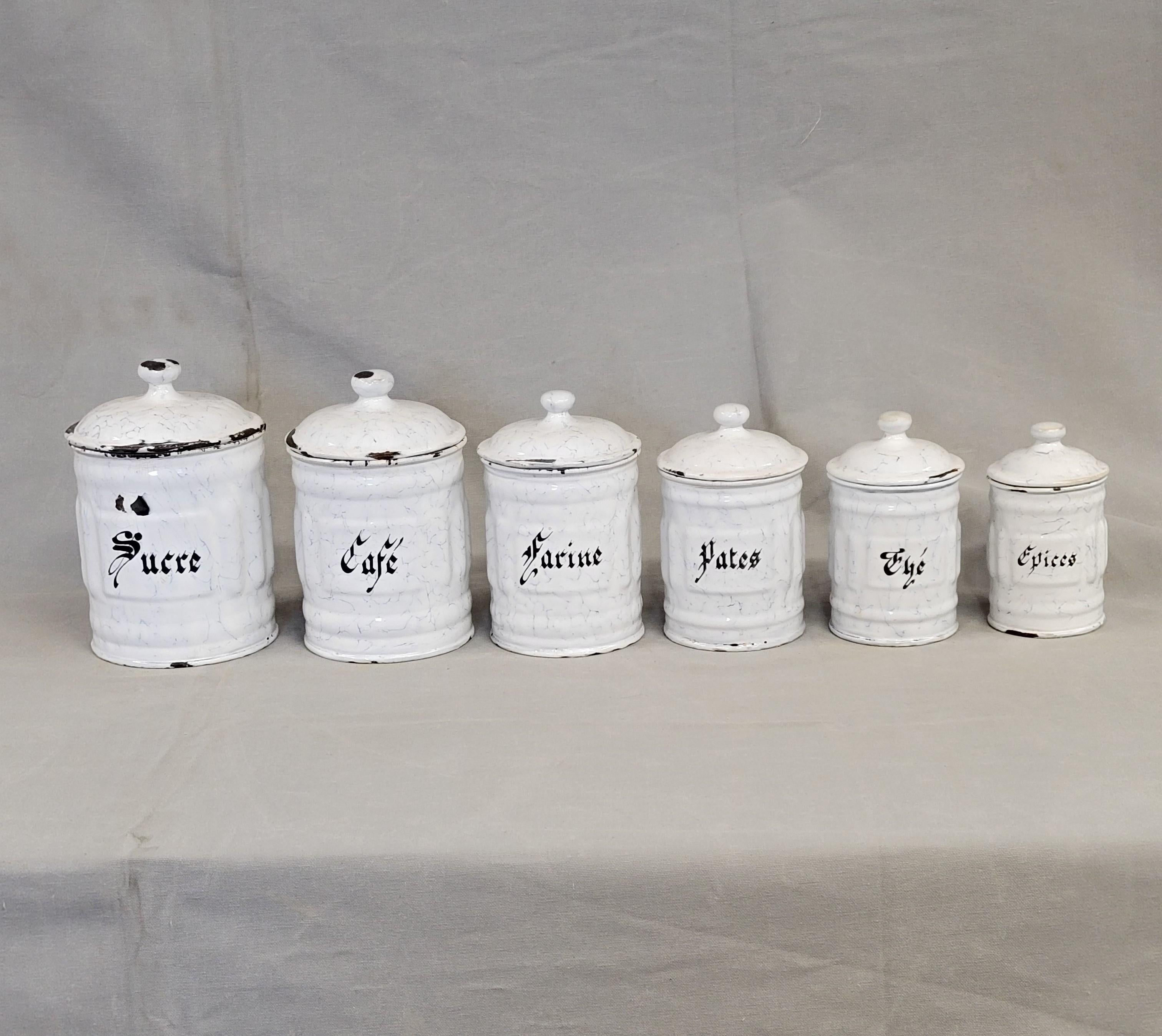 This charming vintage French enamel canister set consists of six lidded canisters. They are white enamel with a hint of pale blue. The black lettering spells out, from large to small: Sucre (sugar), Farine (flour), Cafe (coffee), Pates (pasta), The