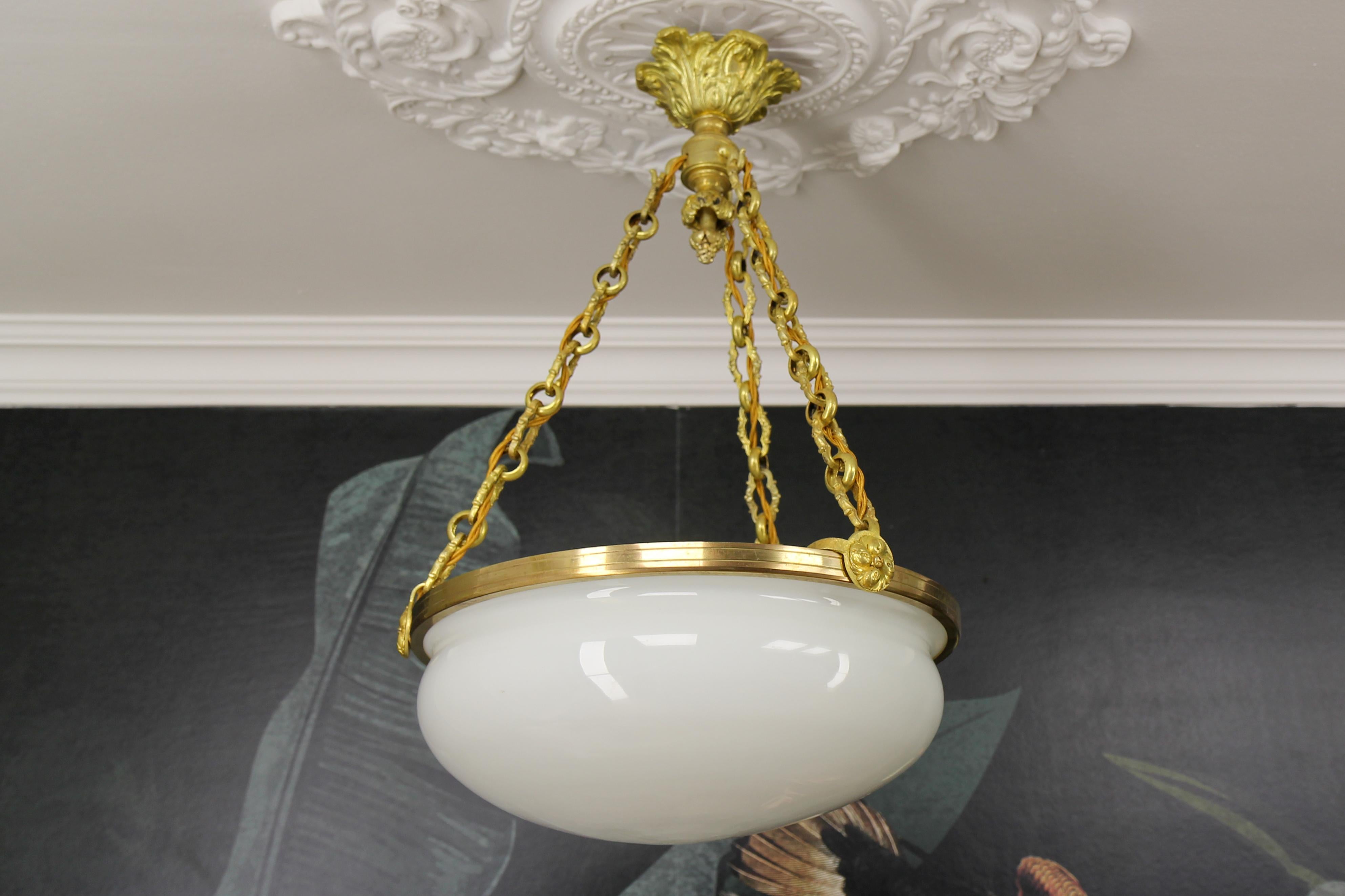 Lustre ancien de style Louis XVI en verre blanc, laiton et bronze, datant d'environ 1920.
Ce magnifique lustre français à trois lumières est composé d'un abat-jour en verre blanc fixé par un anneau en laiton et suspendu à des chaînes en bronze