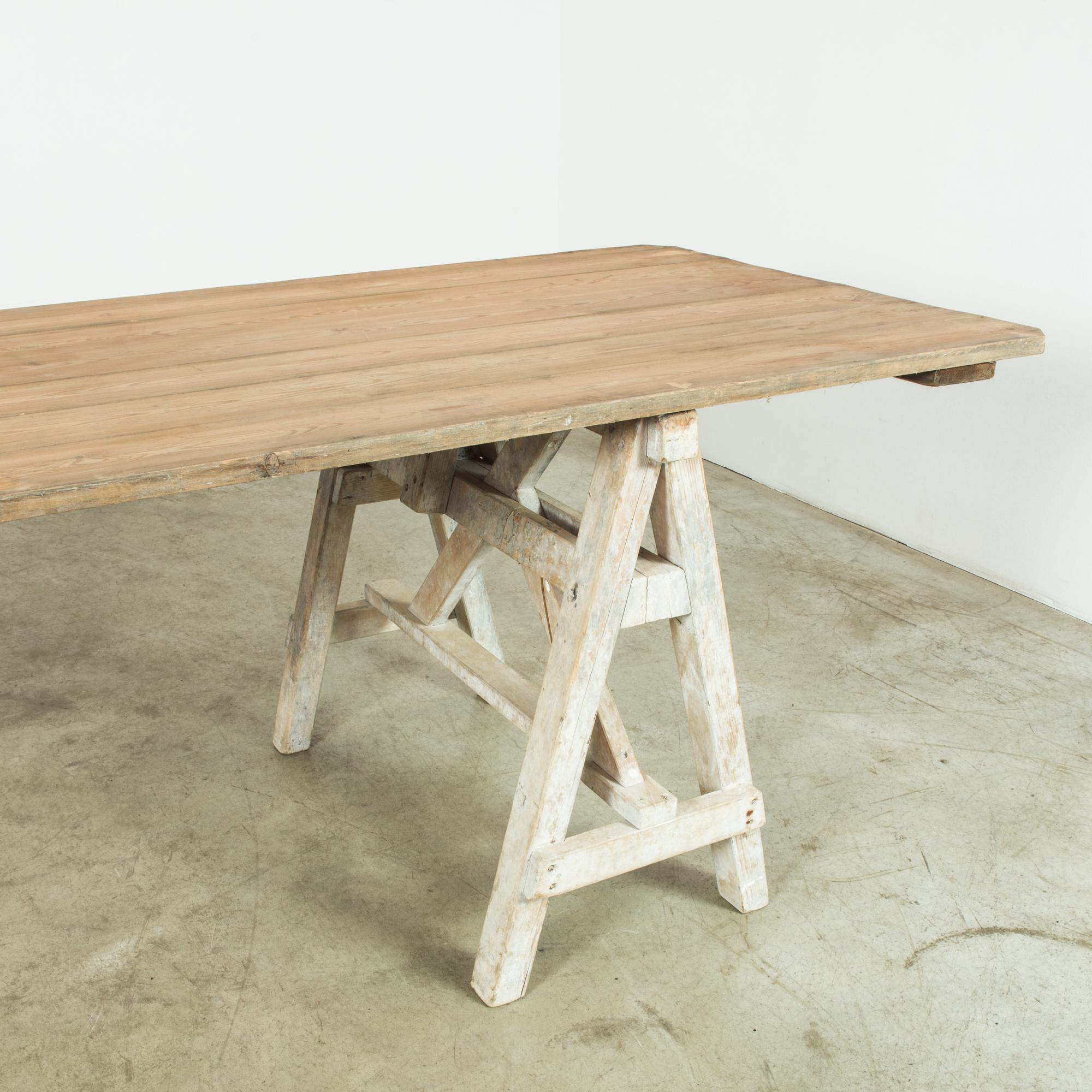 This wooden table was made in France, circa 1900. The wooden planks of the elongated tabletop lend a robust ambience, echoing the past through a superb time-worn patina. A-shaped wooden trestles provide support on both sides, finished in an airy