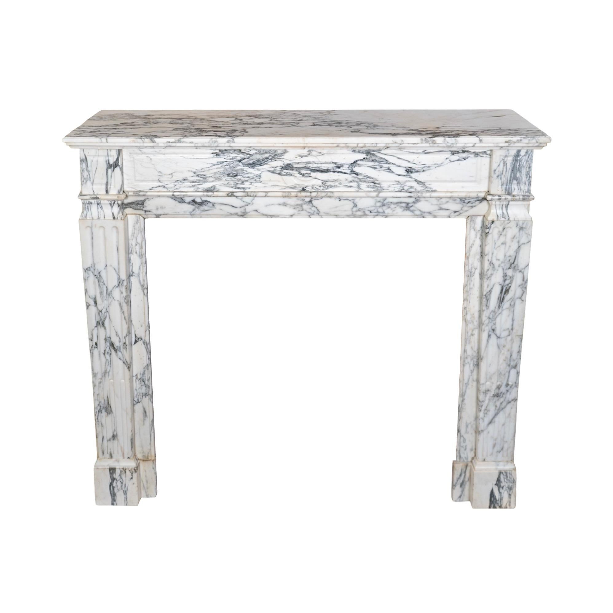 Una antigua repisa de estilo Luis XVI recuperada y elaborada con mármol de Carrara veteado en blanco, procedente de Francia en la década de 1880. Esta exquisita pieza presenta un detalle circular tallado en el centro de la clave, mientras que ambas