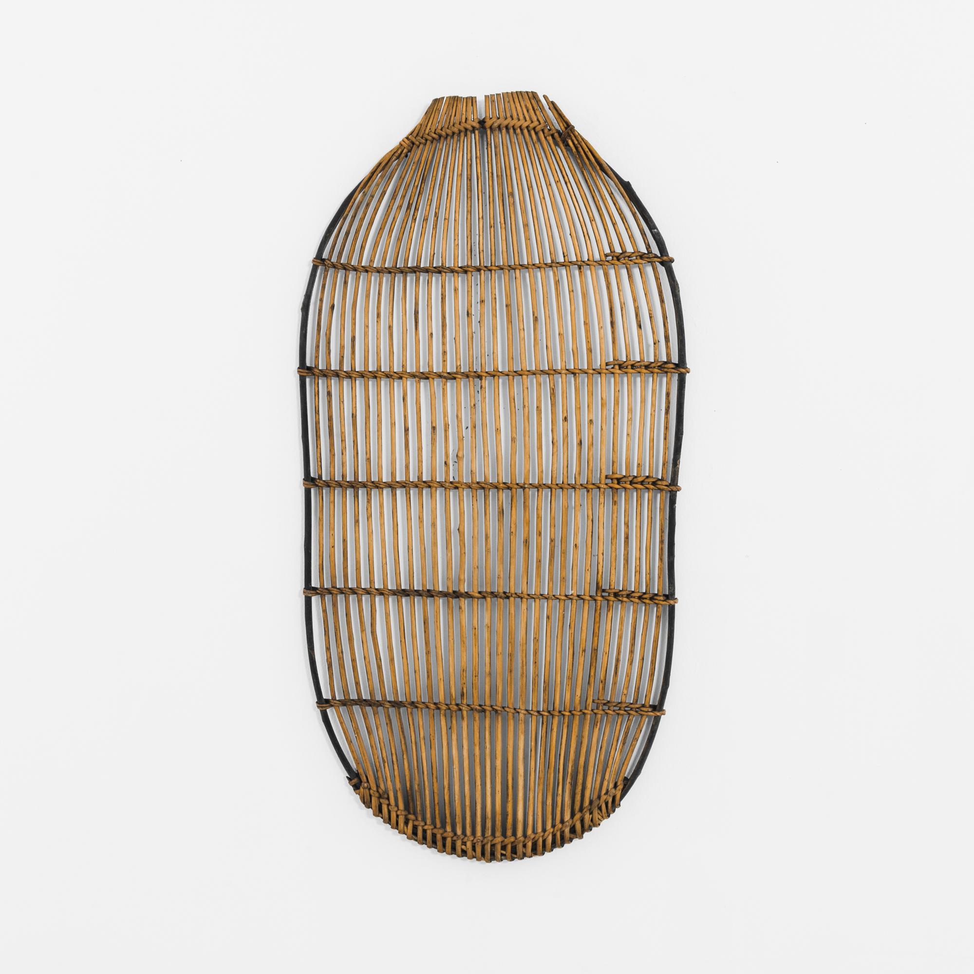 A wooden wall decoration from 1880s France. An oval frame is woven with long pieces of wicker cane, creating an open-weave lattice. The organic lines of the shape and the natural finish of the materials create an aesthetic both rustic and abstract: