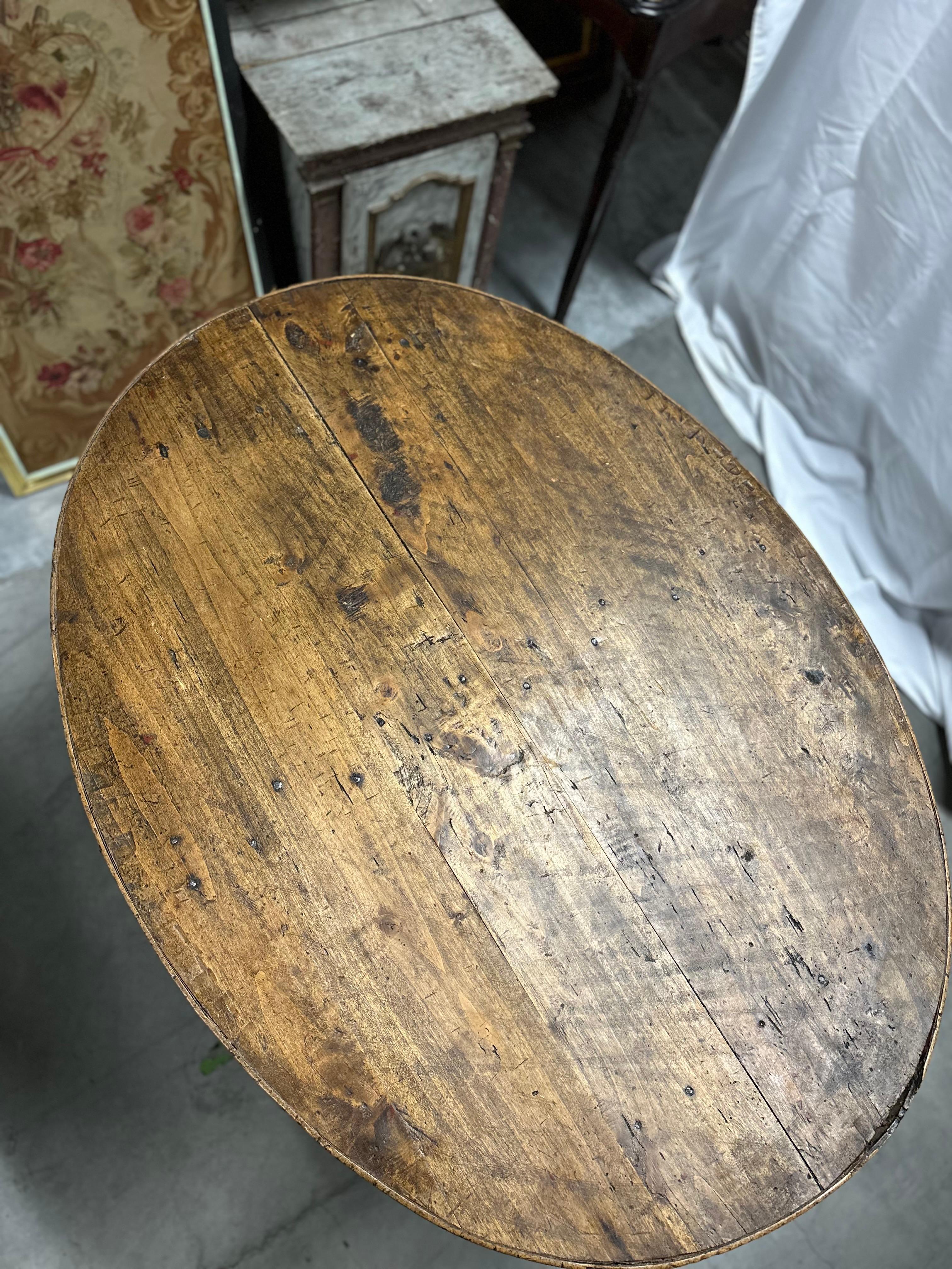 This French Country oval wine tasting table, also known as a tilt-top table, is a splendid example of rustic elegance. Crafted from solid wood, its substantial and sturdy base provides exceptional stability. What truly sets this piece apart is the
