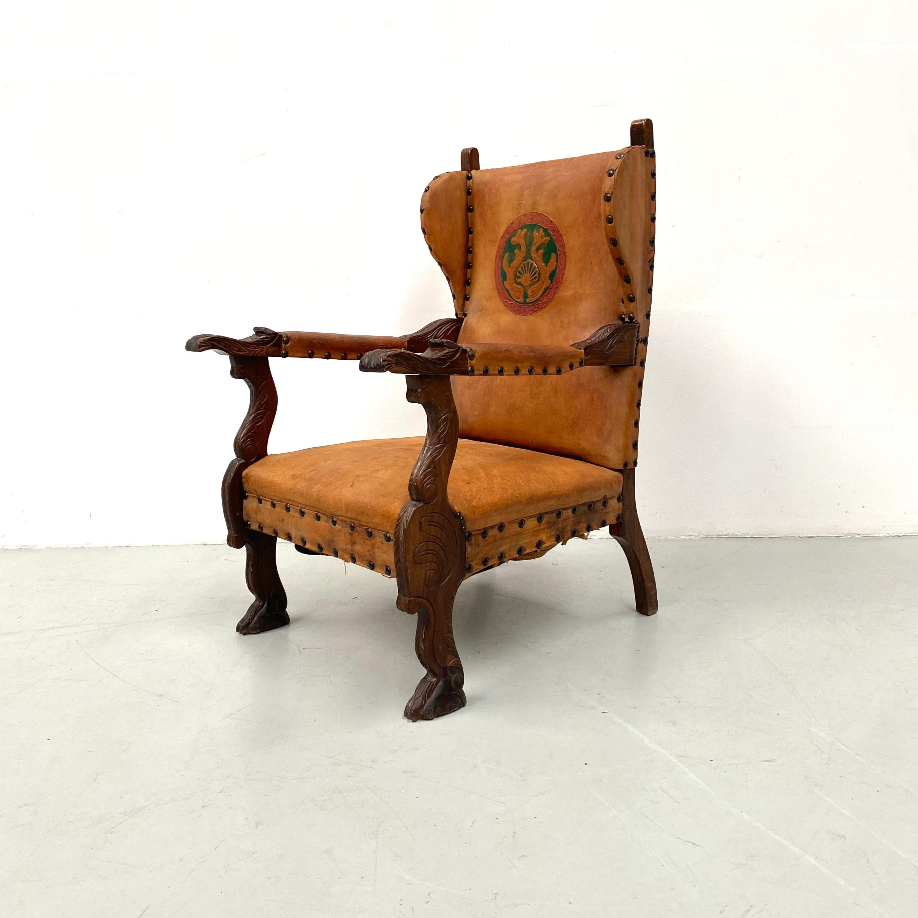 Antique French wingchair in cognac leather with flower and abstract carvings in the oak legs. In the backrest you will find the coat of arms of a noble family from France. Still in good condition. 