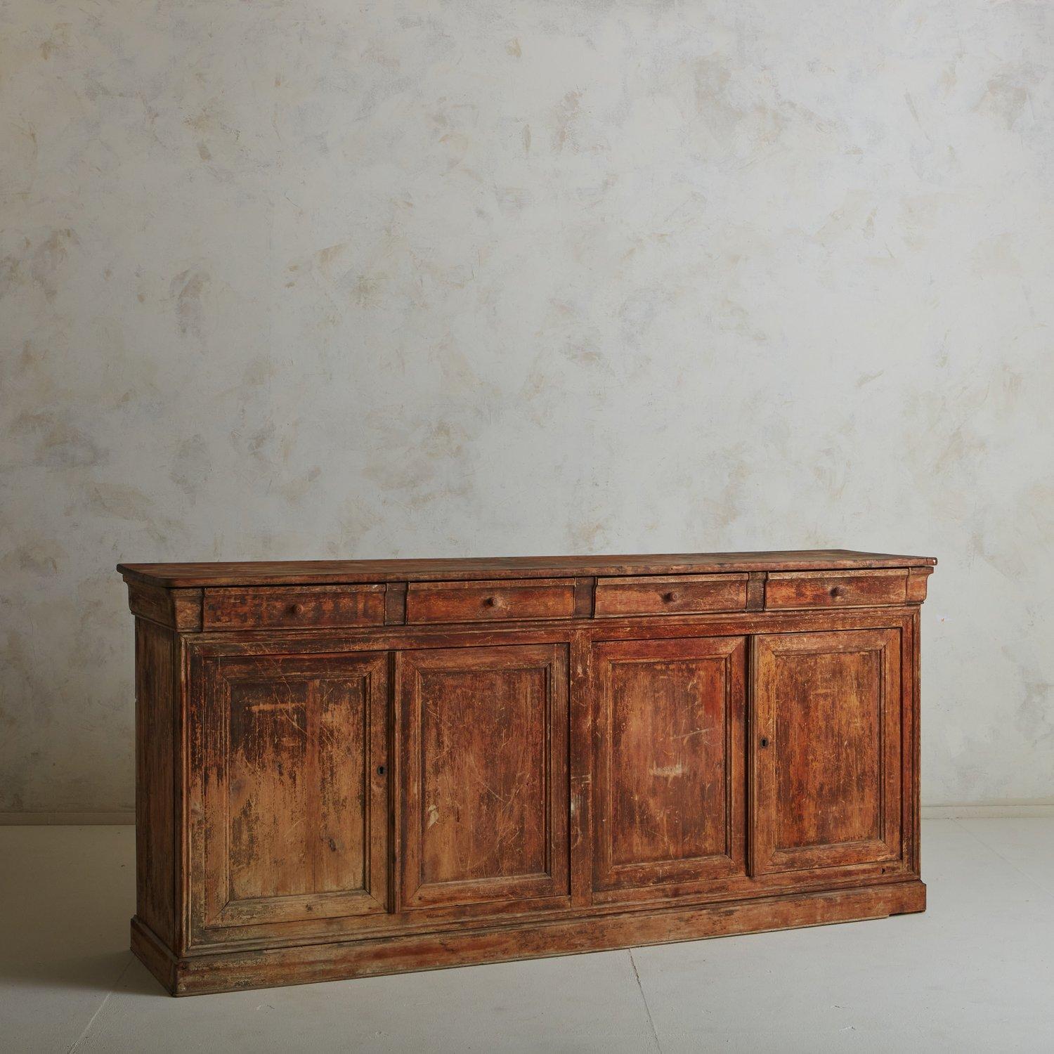 A large scale antique wooden cabinet or counter sourced in France. This piece was constructed with wood and features a stunning patina, rich with history and indications of use. It offers significant storage space, with four front doors which open