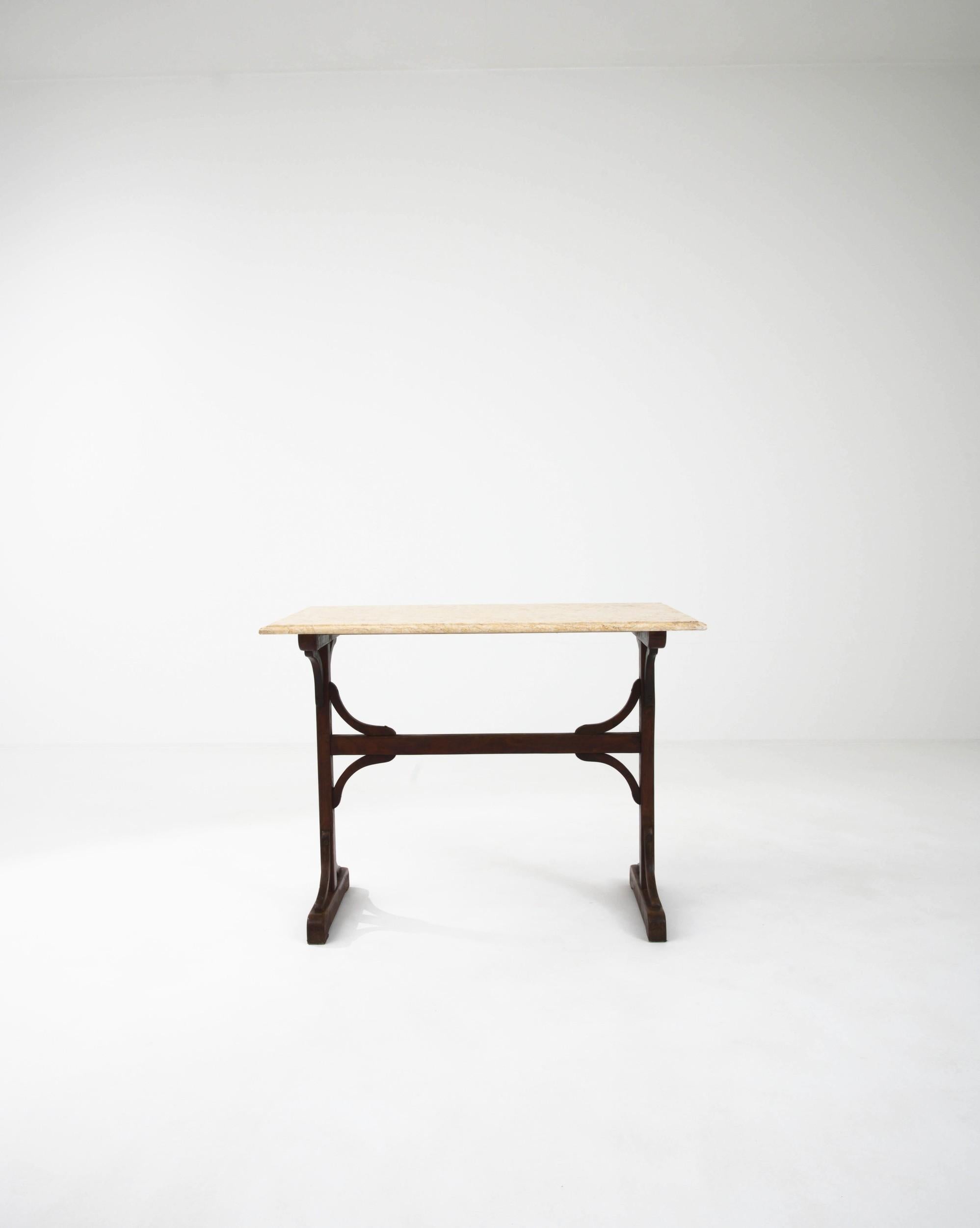 The unique design of this vintage side table makes a compelling find. Built in France at the turn of the century, a marble tabletop sits atop a wooden trestle frame. Bold lines are softened by rounded edges; the sinuous curves of the brackets create
