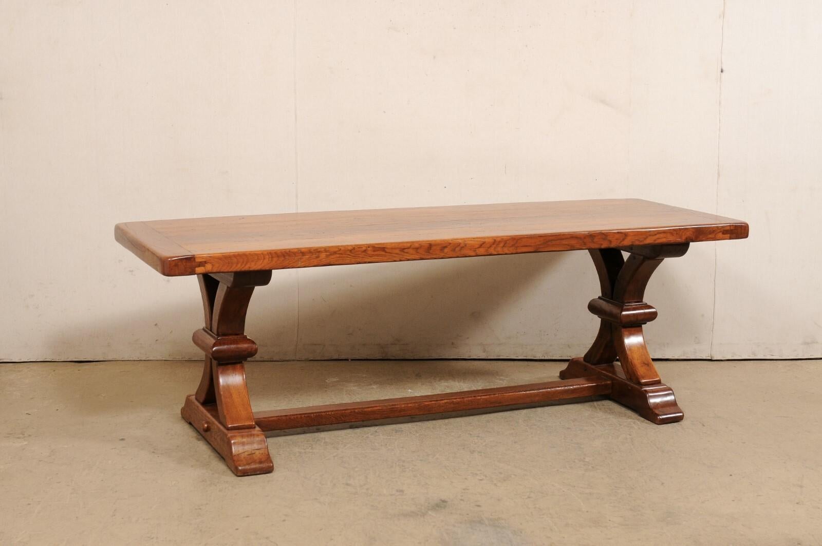 A French trestle leg dining table from the 1920s-1940. This elegant antique table from France has a rectangular-shaped top, just over 7 feet in length, which is presented upon a pair of beautifully-carved trestle style legs that are raised upon rail