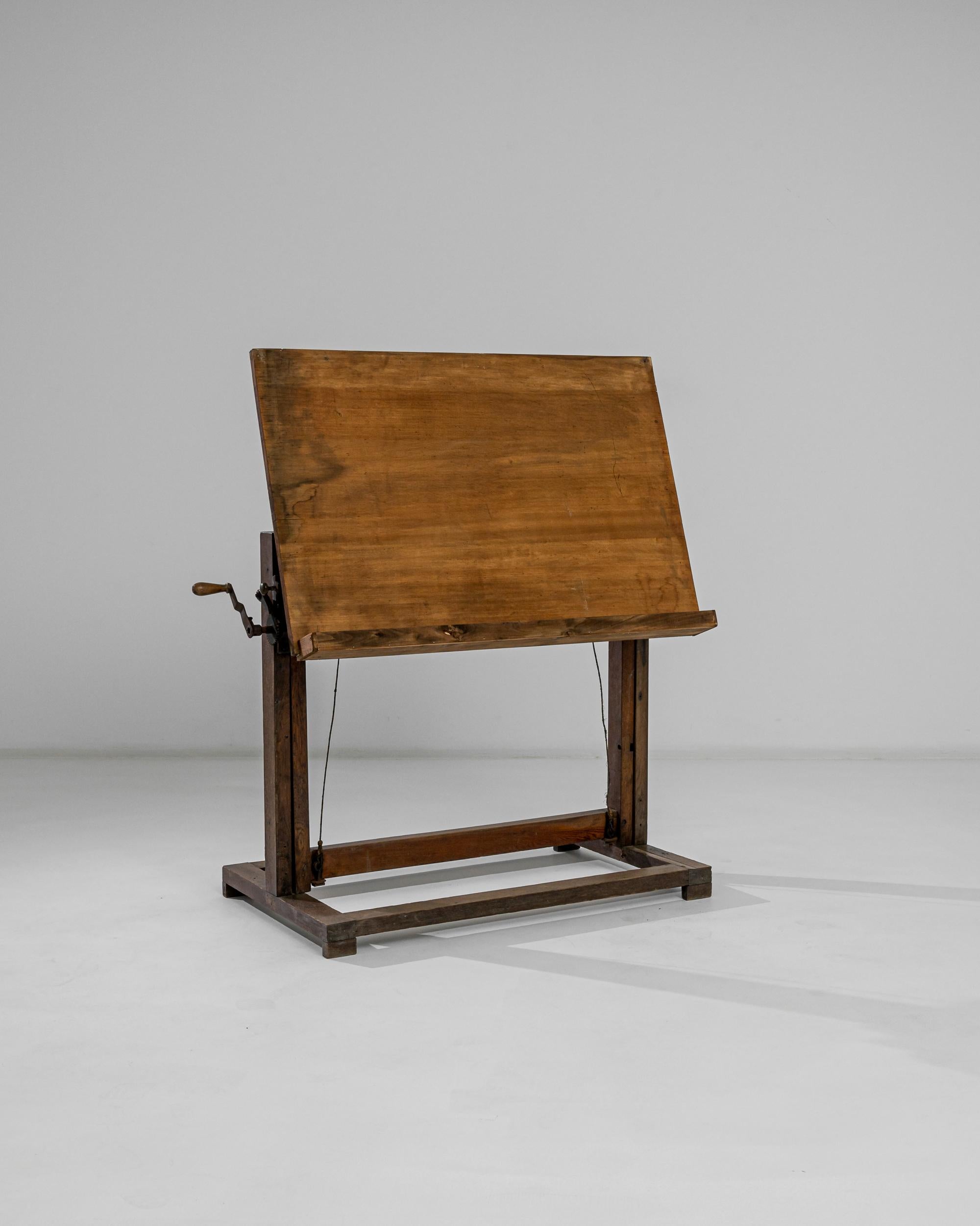 A wooden drawing table made in France circa 1920. This vintage drafting board features an adjustable drawing surface, which may be set at a variety of angles and heights with the help of a crankwheel mechanism. The rectangular shape of the feet