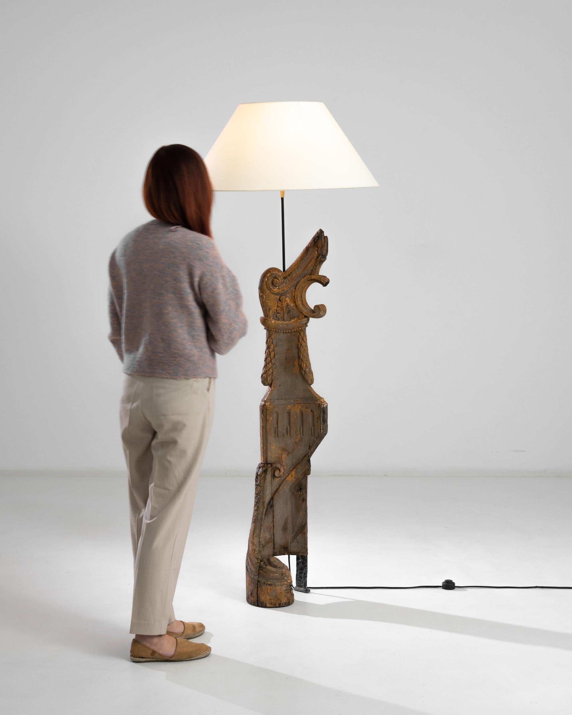 A wooden and metal floor lamp from France, produced circa 1800. At a height slightly under six feet, this tall floor lamp will both illuminate while animating the imagination. The abstract figure carved out of wood, looks like an image of an ancient