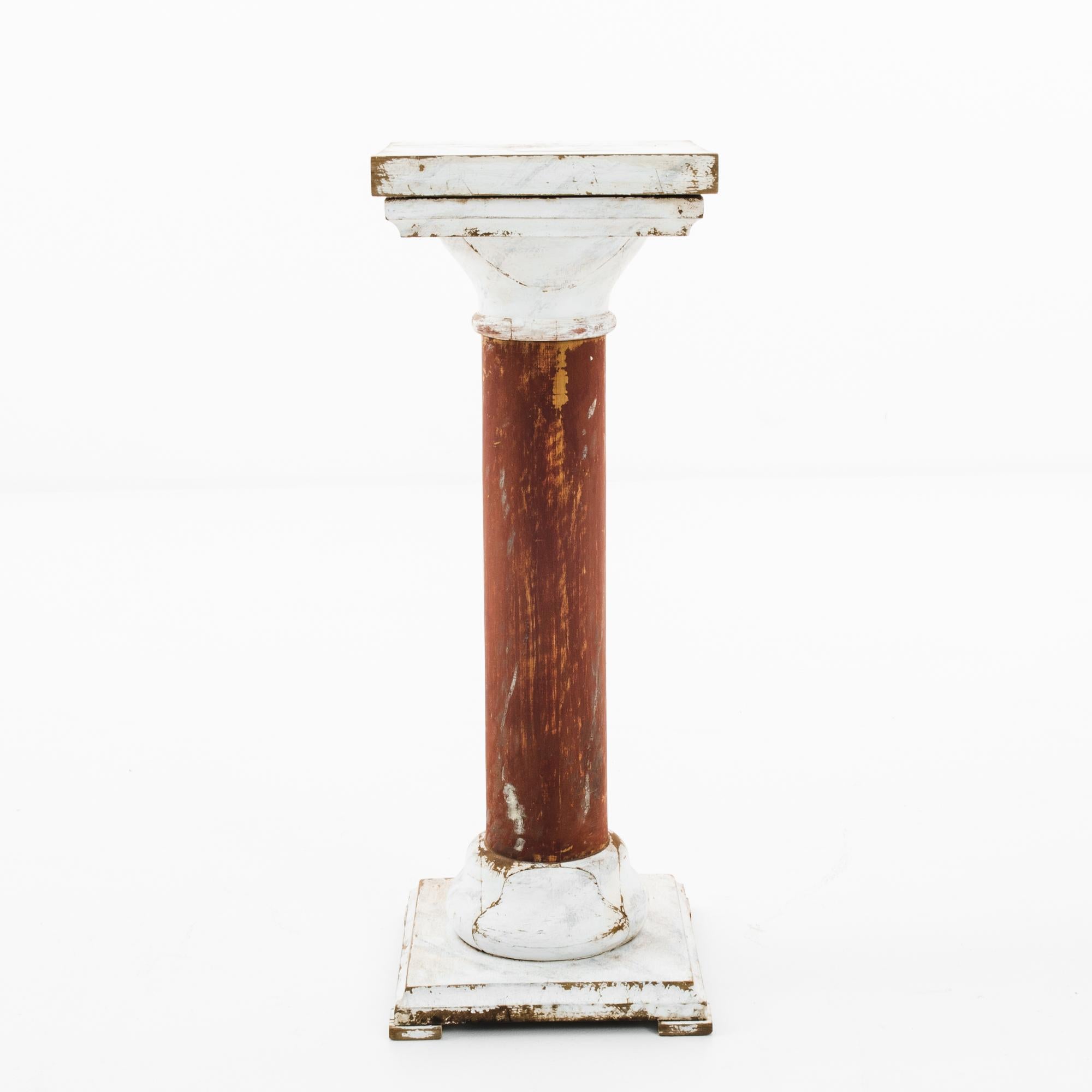 This antique wooden pedestal was made in France. It features a simple, cylindrical stand with a stepped top and base. With a seasoned white and umber patina offering a rustic elegance, this pedestal will imbue a French countrybambience to any space.