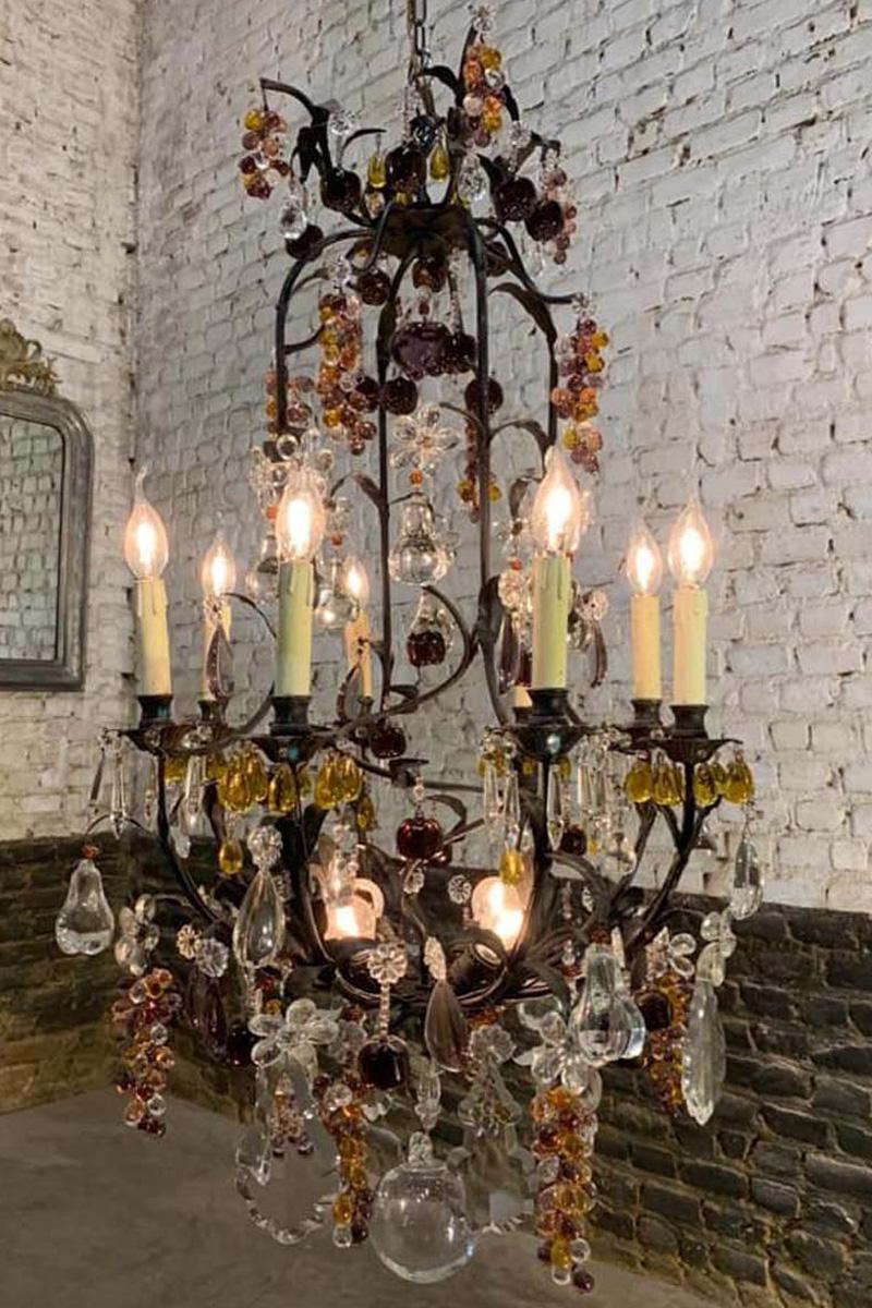 A beautiful large Art Nouveau fruit chandelier that was made in France, circa 1900.
It has a blackened wrought iron open cage frame with leaves that suspend the crystal pendants. The chandelier is decorated with multicolored fruit. It features clear