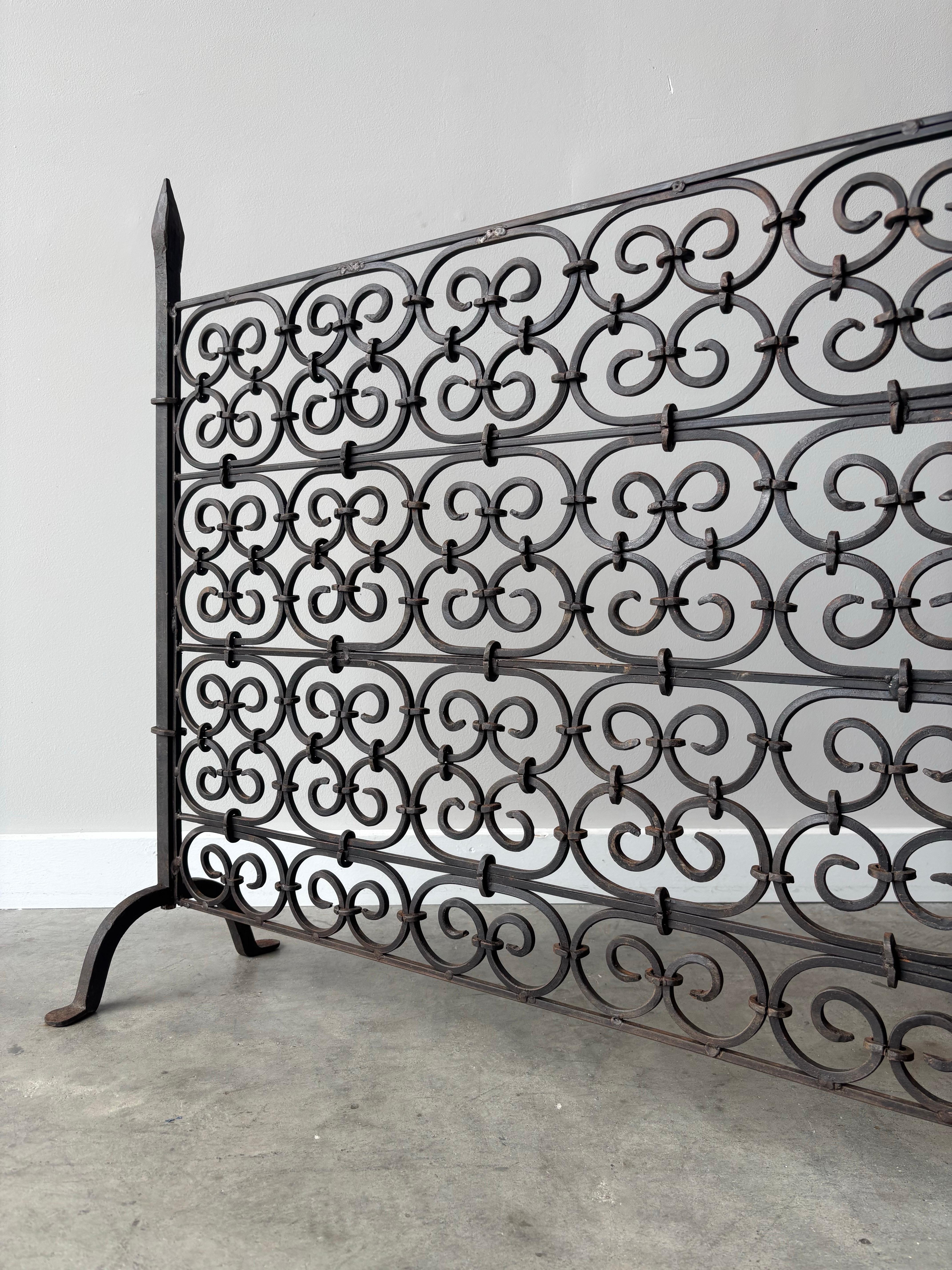 Questo eccezionale paravento per caminetto in ferro battuto forgiato a mano mette in mostra la maestria degli artigiani francesi del metallo. Caratterizzato da intricati motivi a volute gotiche che danzano sulla superficie, questo pezzo trasforma
