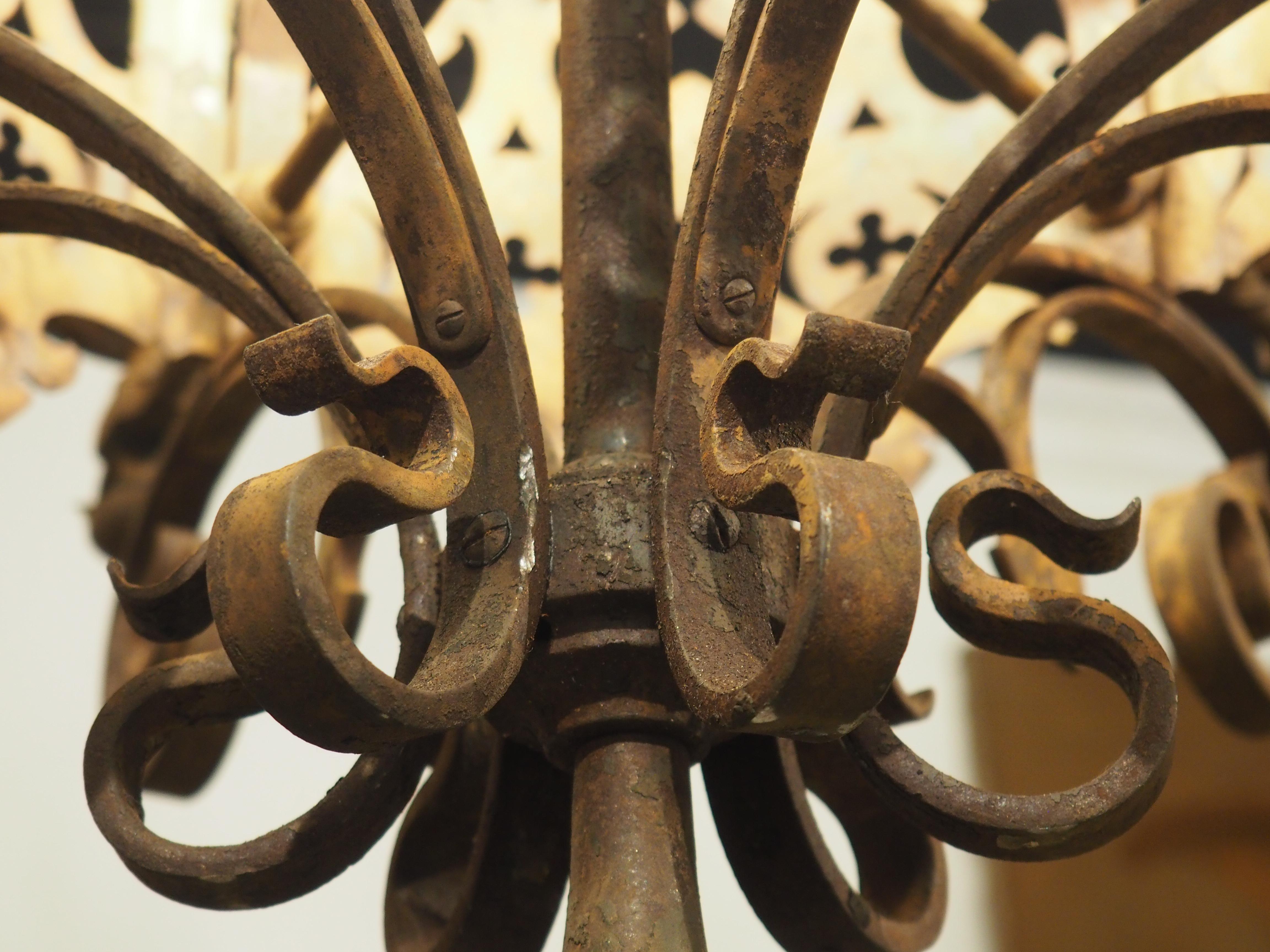 Dating to the latter half of the 19th century, circa 1880, this French wrought and pinned iron chandelier is in the Gothic style, as evidenced by the highly detailed ring that comprises the bottom bowl. A pierced ring adorned with a repeating