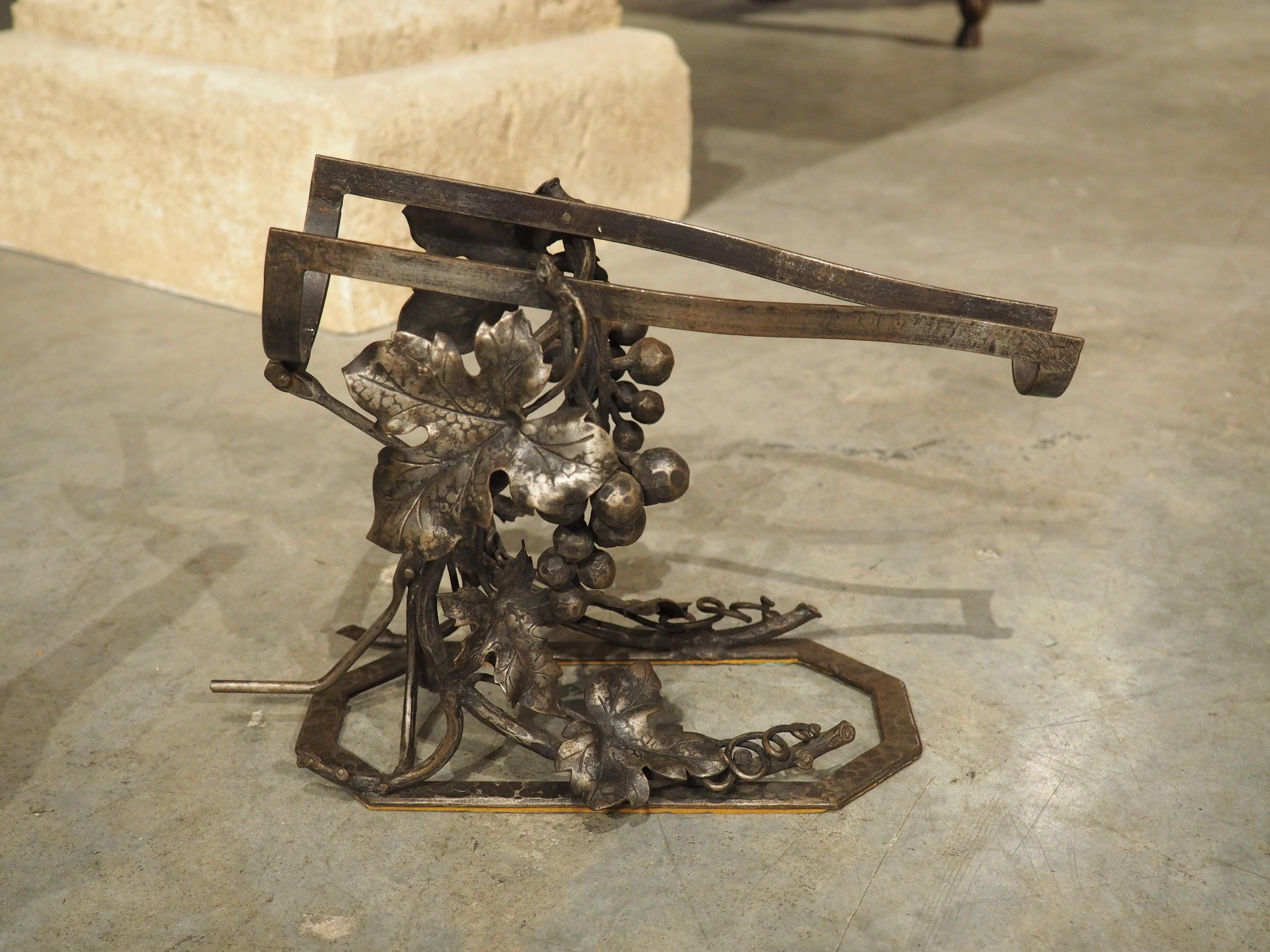 A charming wrought iron wine bottle cradle from France, circa 1900, this wine accessory features sprawling grapevines that run up each side, forming legs that are attached to an open octagonal base with a dappled appearance. The cradle is hinged,