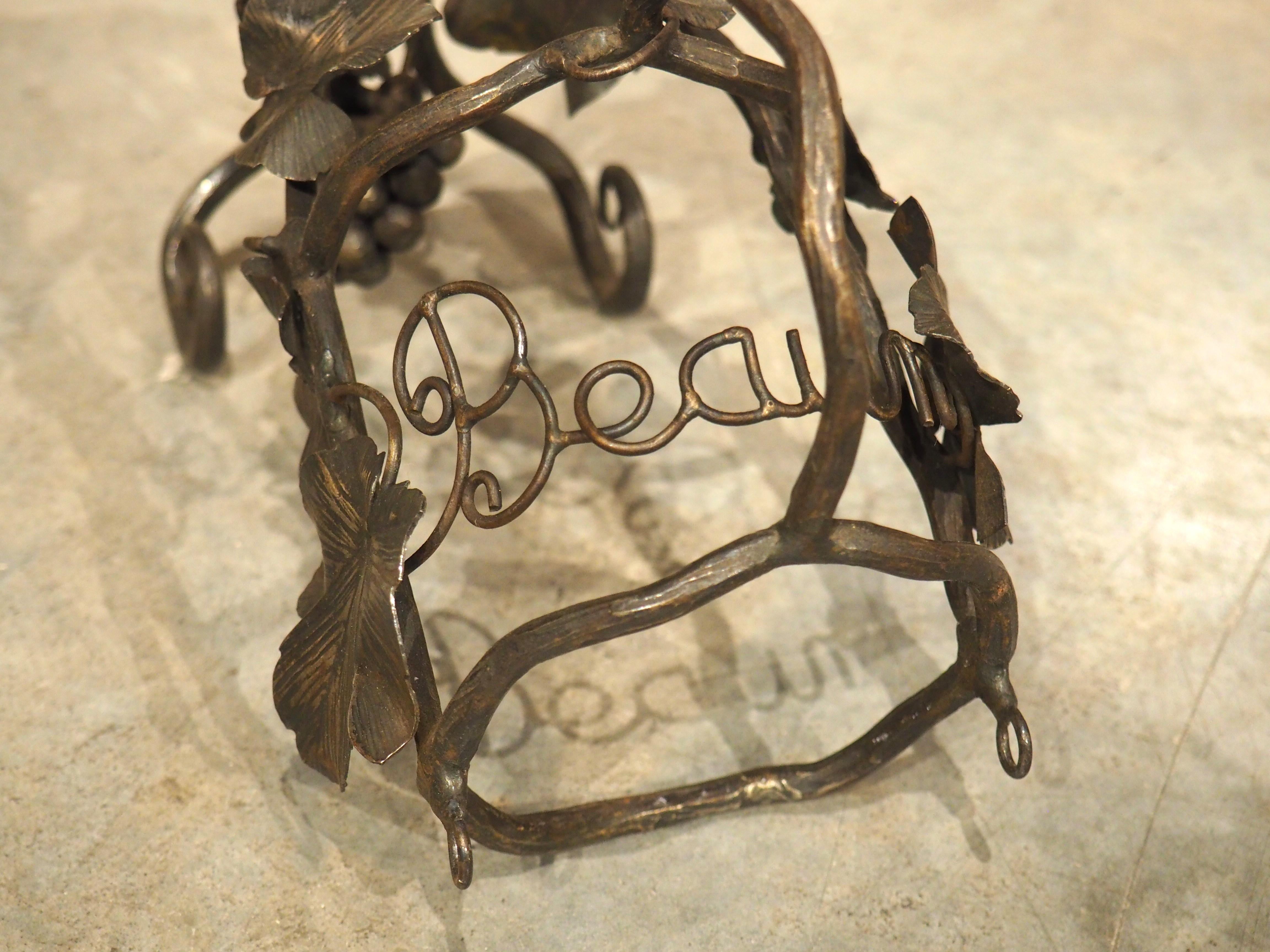 A charming wrought iron wine bottle holder from Beaune, France, circa 1900, this wine accessory features realistically crafted grape bunches, complete with sprawling vines. A pair of volute scrolled feet in the front flank a hanging grape cluster,