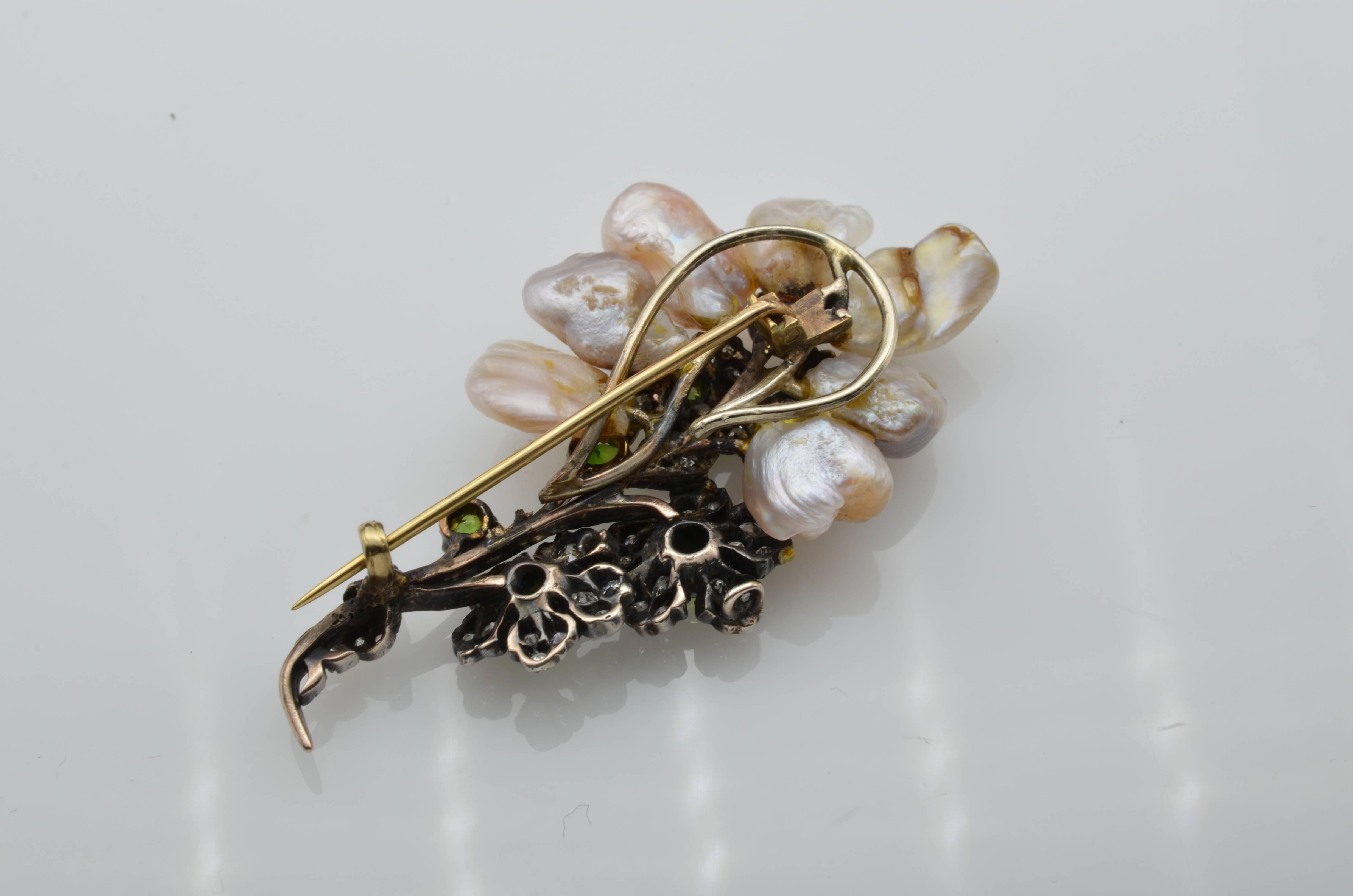 This antique turn of the century brooch is made with natural fresh water pearls in gorgeous colors of peaches, pinks, greys and whites. Green demantoid garnets and bright white diamonds decorate the beautiful blossom branch of the brooch. The