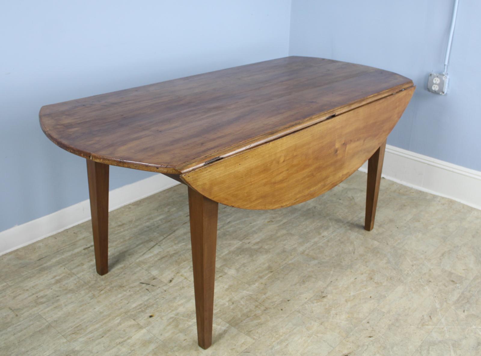 A beautiful warm fruitwood with lovely grain and patina. This oval country farm table has classic tapered legs for a simple and elegant look, and the top has good color. Some early distress on the top and the knuckle which adds lots of character.