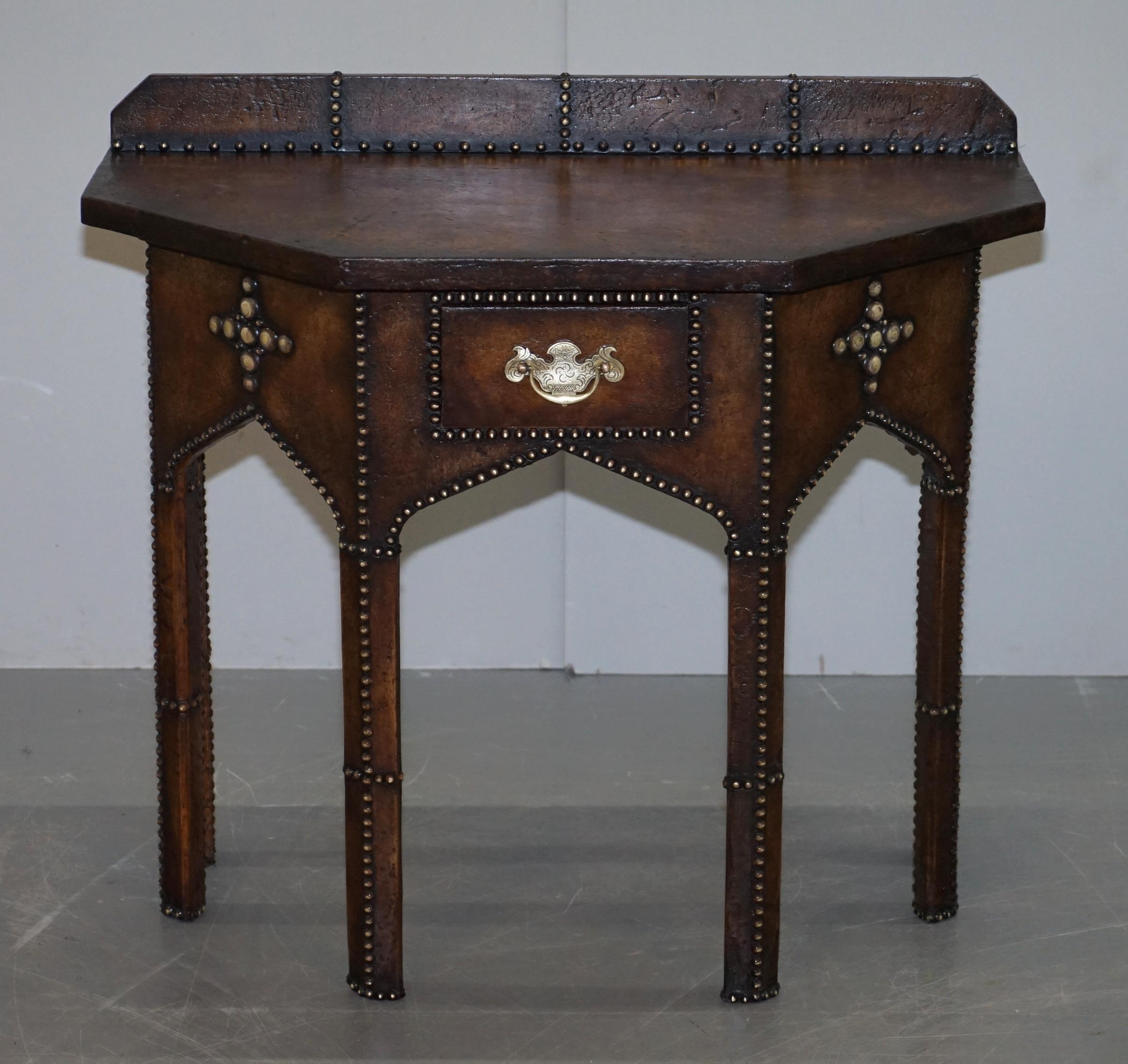 We are delighted to this absolutely stunning one of a kind Gothic Pugin style hand studded brown leather console table with single drawer

This is an exceptional piece of art furniture. It’s made in the Gothic Pugin style as mentioned, it dates to