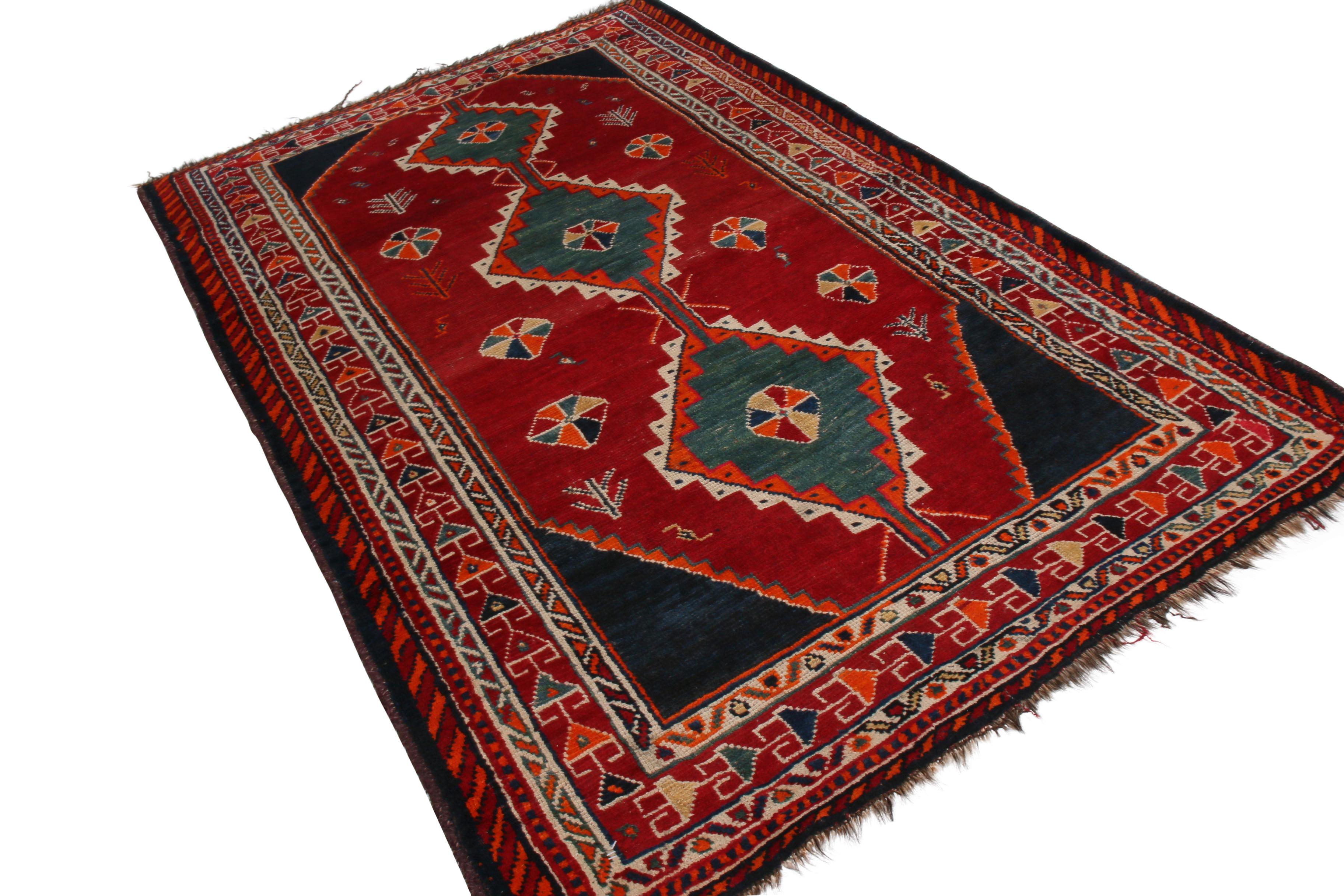 Hand knotted in wool originating between 1900-1910, this antique Gabbeh Persian rug hosts transitional elements with a variety of Classic, rich colorways. The variety of fabulous blue and red in the geometry of the field and border alike draws the