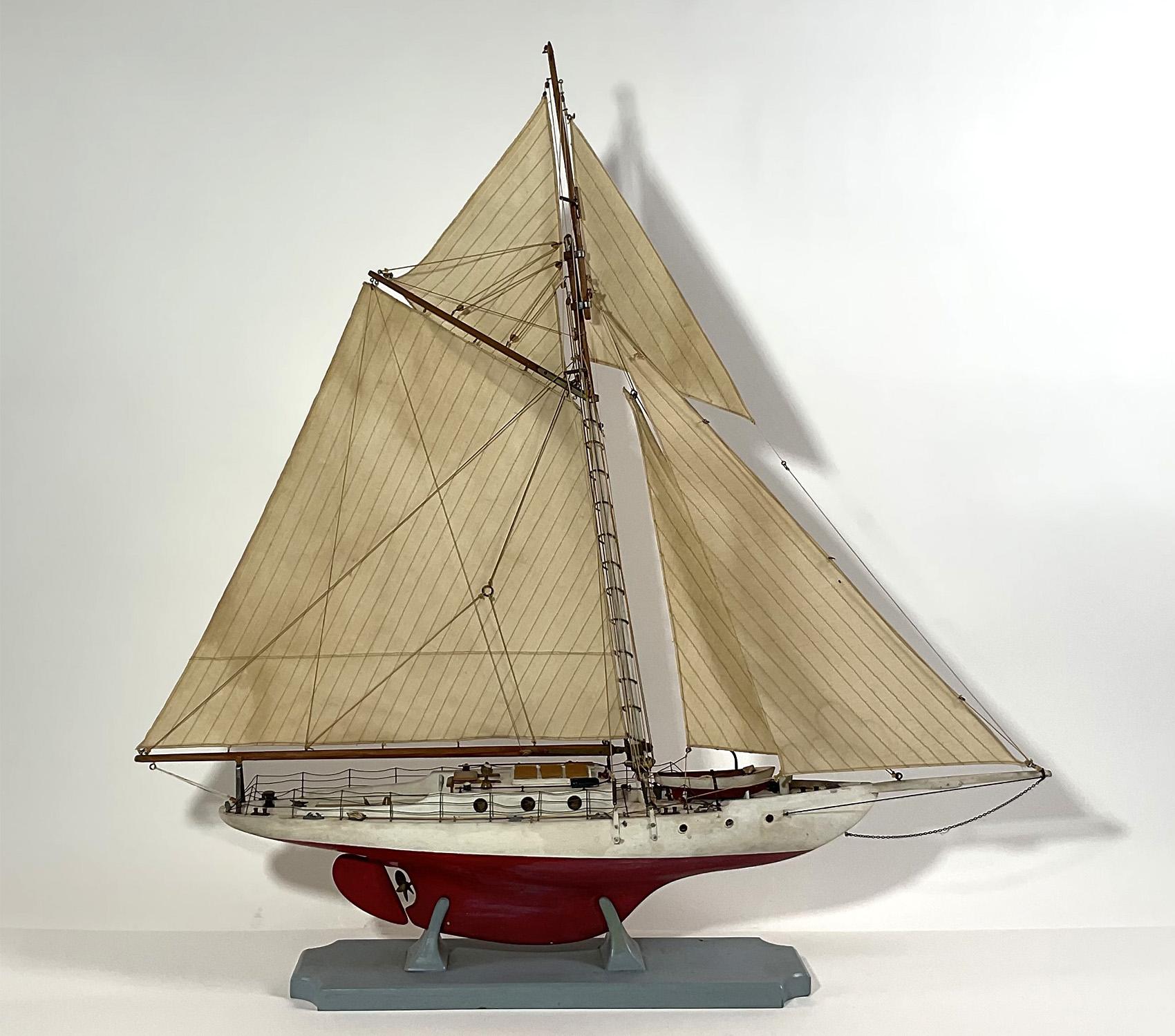 Yacht model with a full suit of sails. Charming model with details including launch, port and starboard lanterns, portholes, skylights, cleats, chocks, binnacle, helm, etc.. Mounted to its original baseboard. Circa 1955.