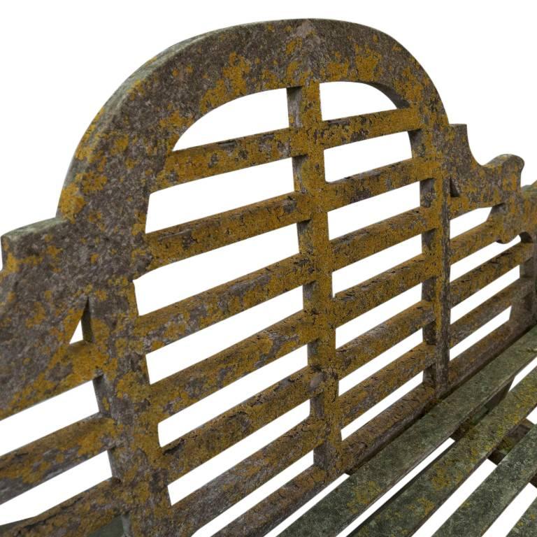 This well crafted garden bench has half circle rounded decorative arm rests and some beautiful green moss among the patina of age and wear.