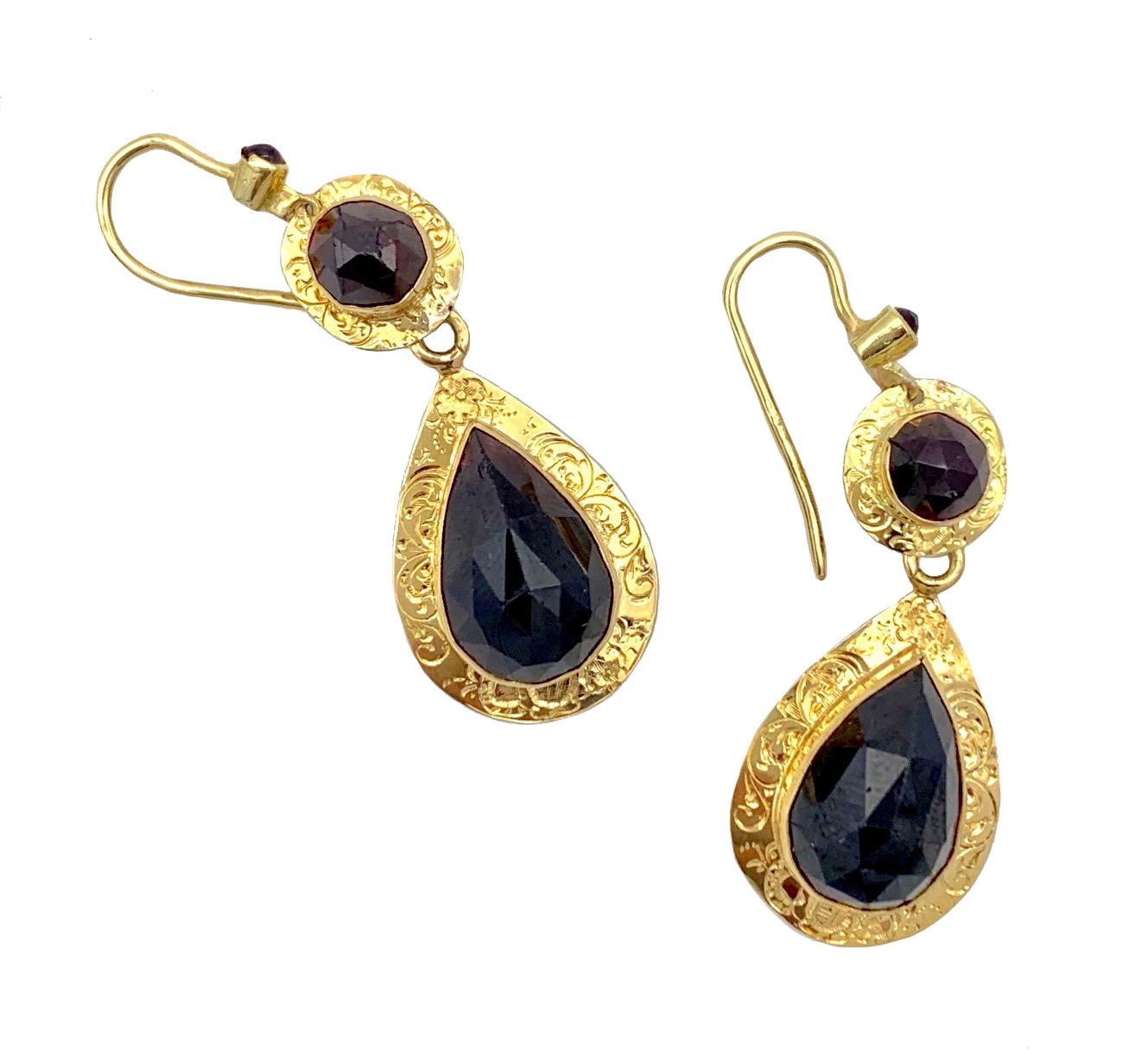 These elegant earrings were handcrafted in 1845 ca. Each earring is set with a small garnet cabochon near the hook. The top round segment is set with a round facetted garnet in an engraved gold mount from which a drop shaped element set with a drop