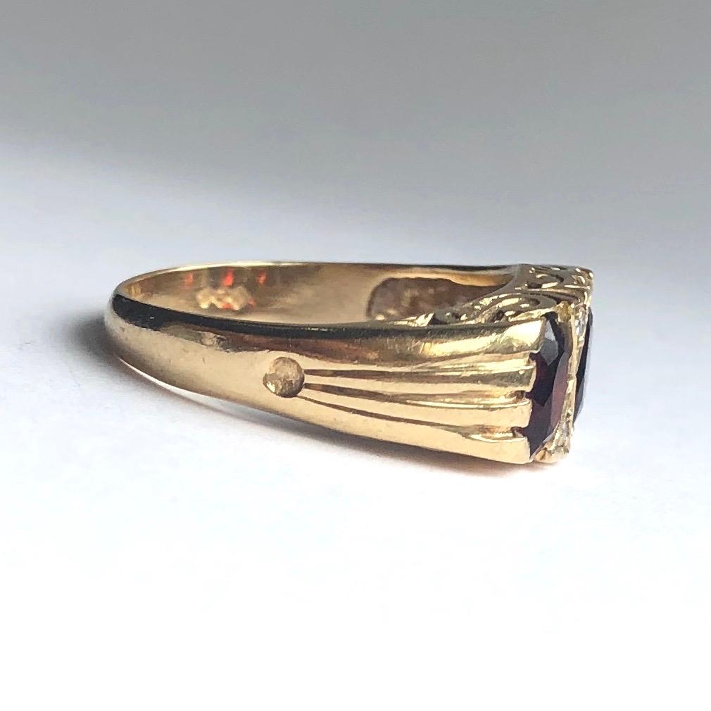 The garnet stones in this ring are deep red in colour and when they hit the sunlight they glow bright red. Either side of the central stone there are pairs of diamonds. The gallery is closed and has scroll detail. 

Ring Size: L 1/2 or 6 
Band