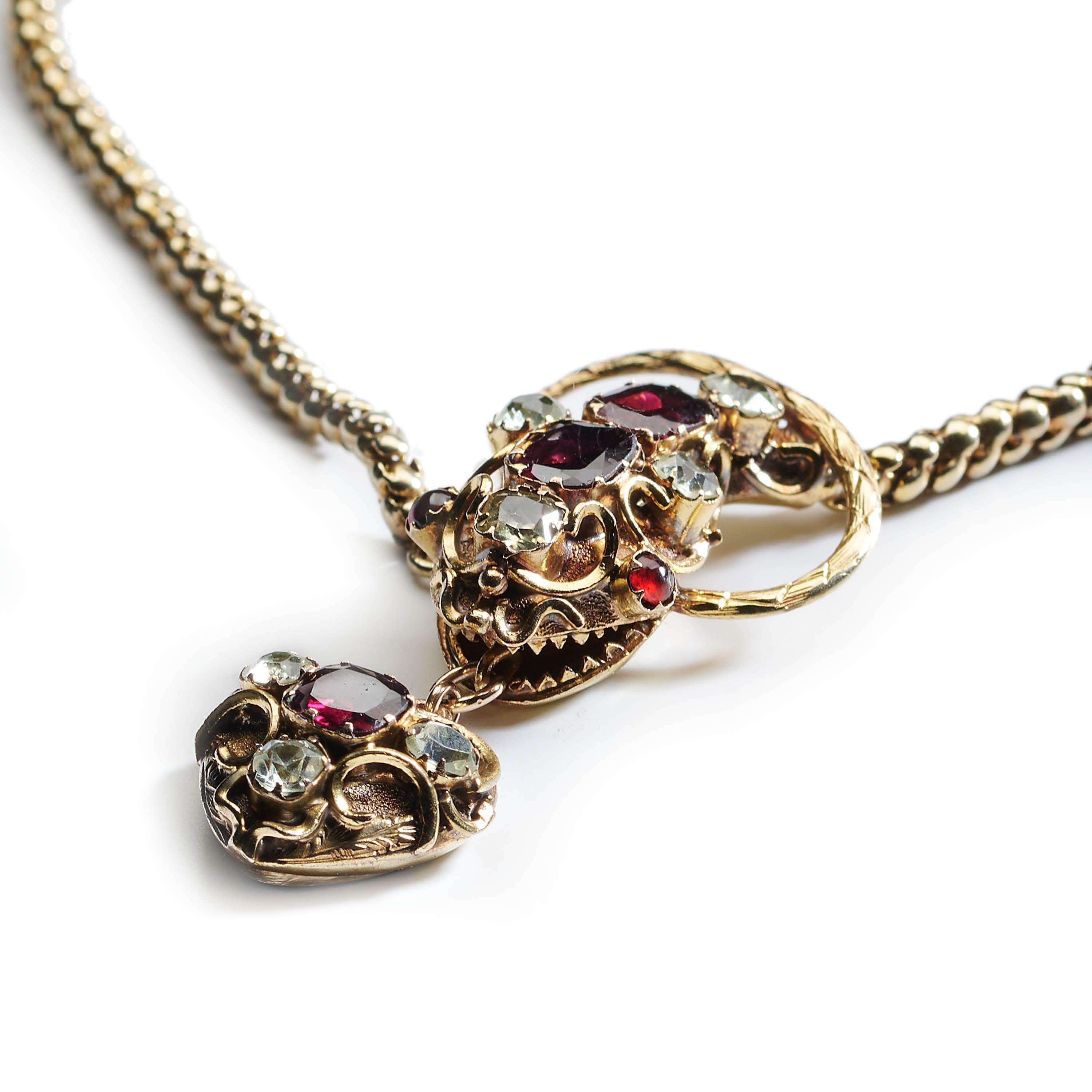 An early Victorian garnet, beryl, ruby and gold snake necklace, with cabochon-cut ruby eyes, with faceted garnets and pale green beryls set in the head and heart pendant, in closed back claw settings, surrounded by scrolling wirework, the mouth is