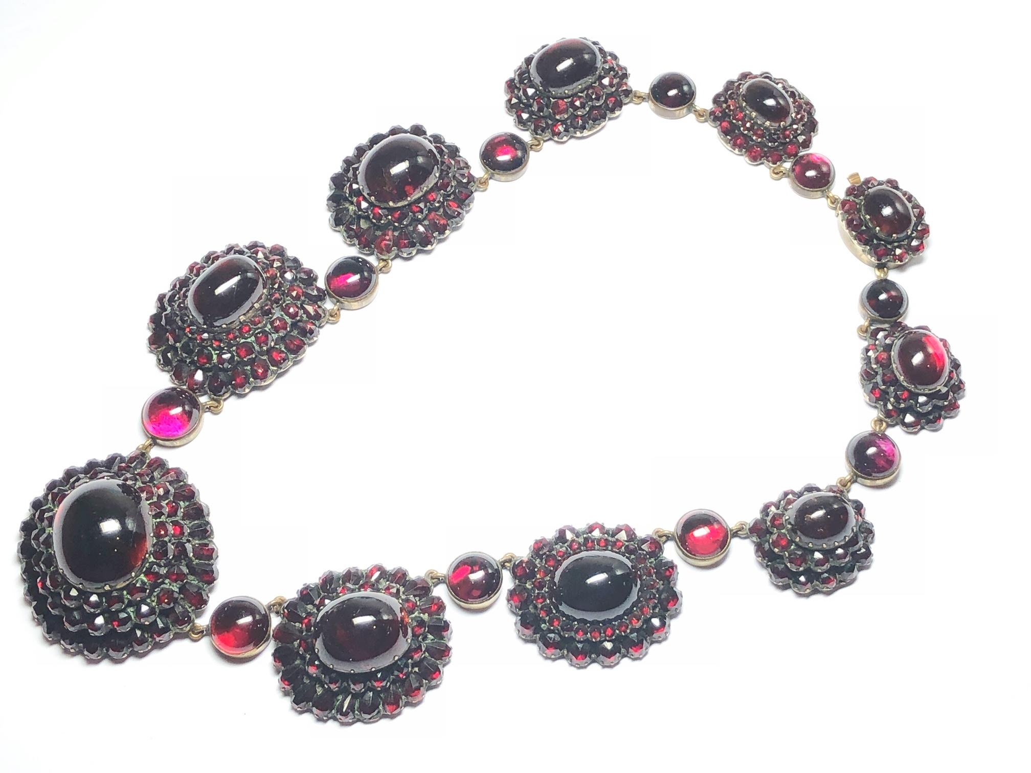 A Victorian Bohemian garnet necklace, with ten graduating clusters, set with cabochon garnets in the centres, surrounded by rows of round and pear shaped, rose-cut garnets, mounted in closed back silver gilt, with cabochon garnet spacers in
