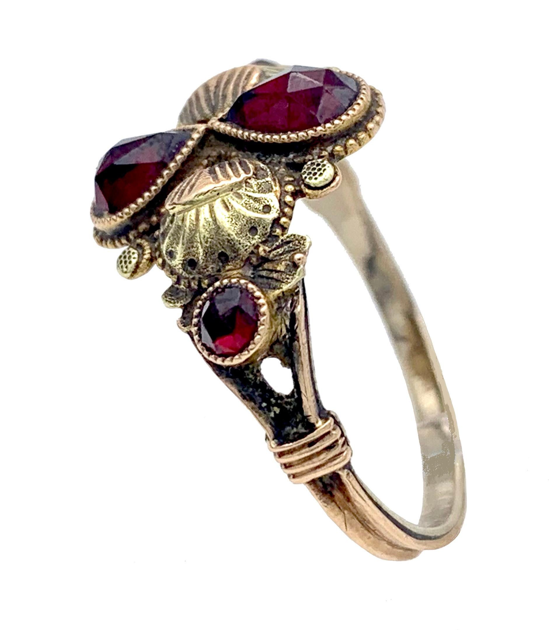 This delicate Georgian ring has been worked in 14 karat gold 'à trois couleurs' and features two drop shaped facetted garnets within an engraved red gold border symbolising an eternity loop and butterflies with round cut garnets as bodies. 