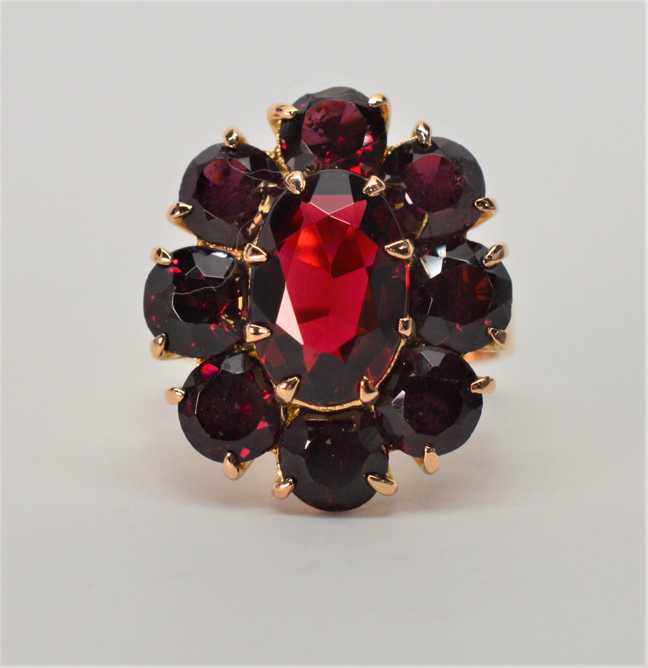 More than twelve carats of deep rich natural hand-cut garnet stones illuminate this spectacular antique cluster ring made of fourteen karat (14K) yellow gold. The oval ring head measuring approximately 23.25mm x 26.25mm has an oval faucet center