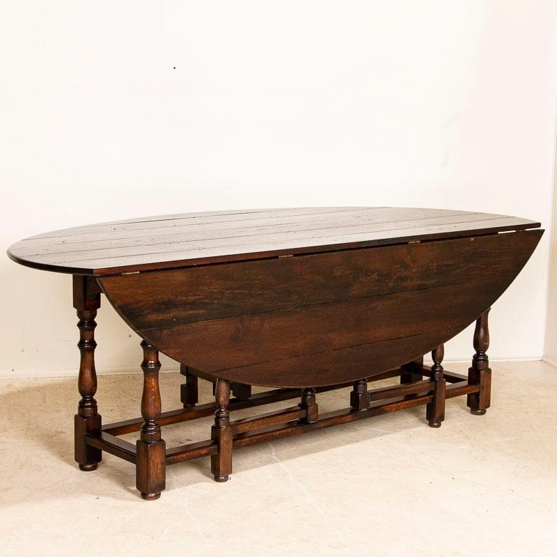 This striking gateleg dining table is also known as an English wake table with drop leaves. Notice the rich brown patina of the oak, aged and naturally distressed over generations of use and lovely turned legs. The large oval shaped top has 2 drop