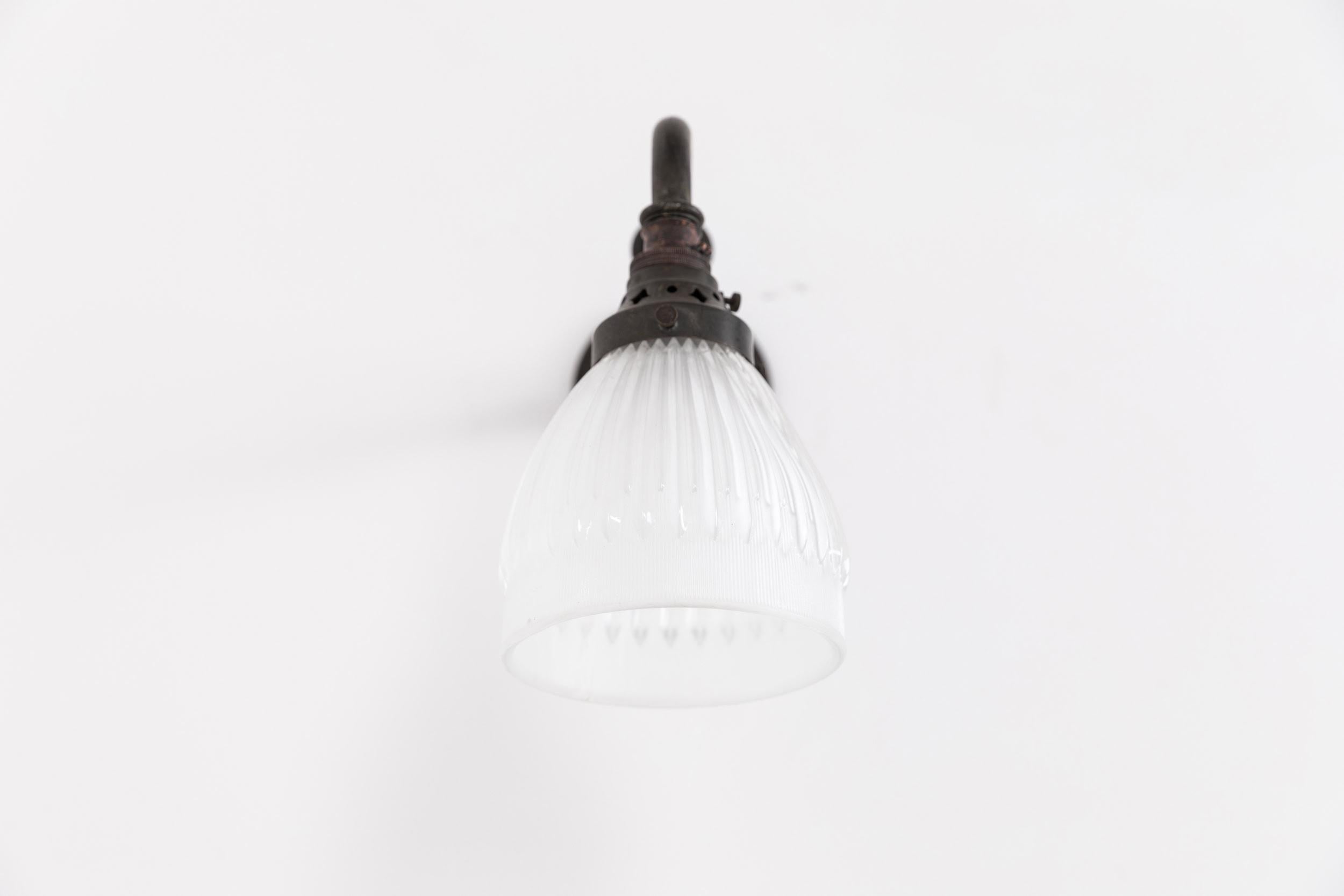 

An incredibly elegant wall mounted light made in England by Holophane. c.1920

The prismatic glass 'Residence Reflector' shade made by Holophane, stamped to rim, and simple brass swan neck wall bracket with attractive dark patina and