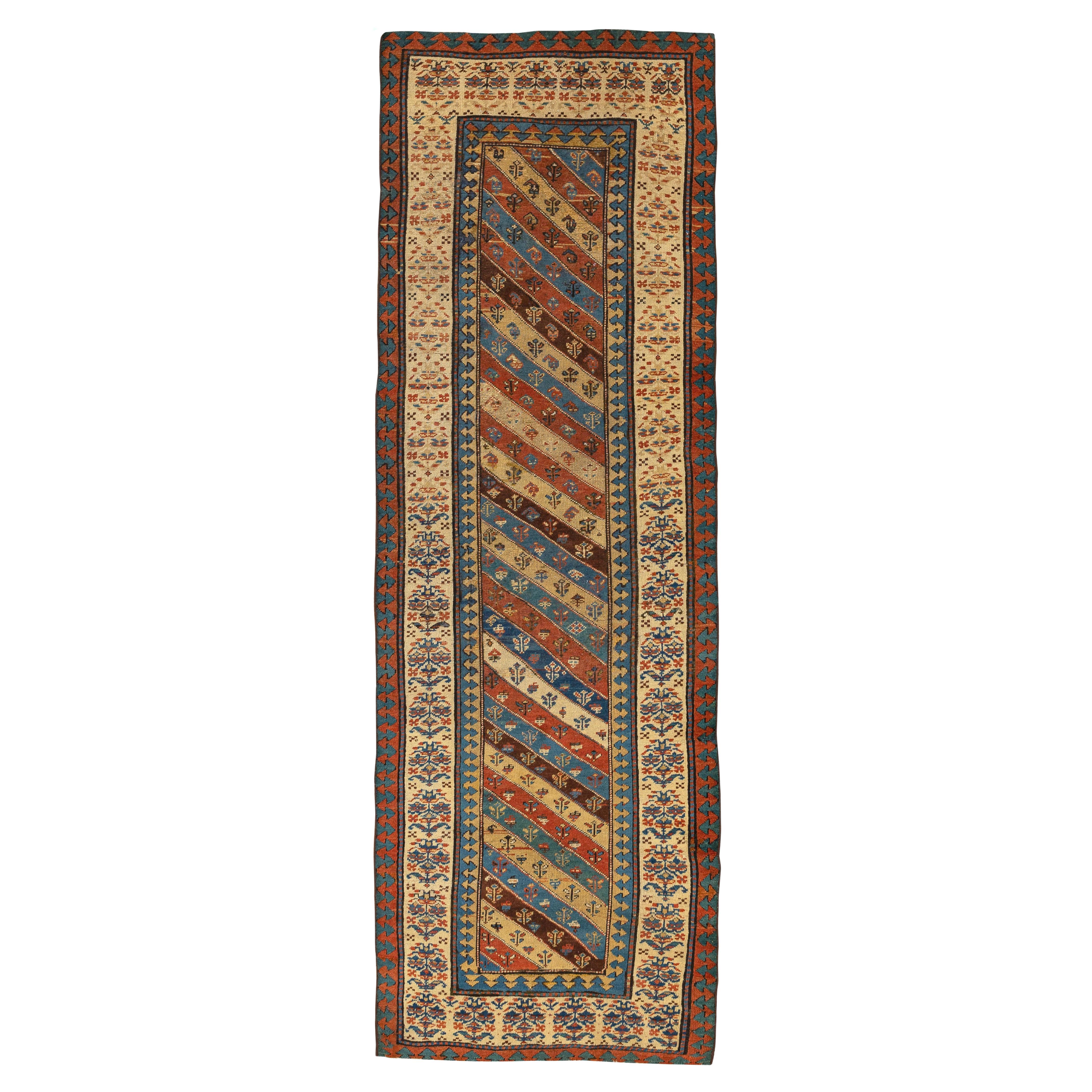 Gendje – South Caucasus 
This Gendje rug from the mountainous region features a delicate diagonal stripe design. The stripes are populated with floral motifs and geometric figures in dazzling colours. Its striking shades of blue, red, indigo and