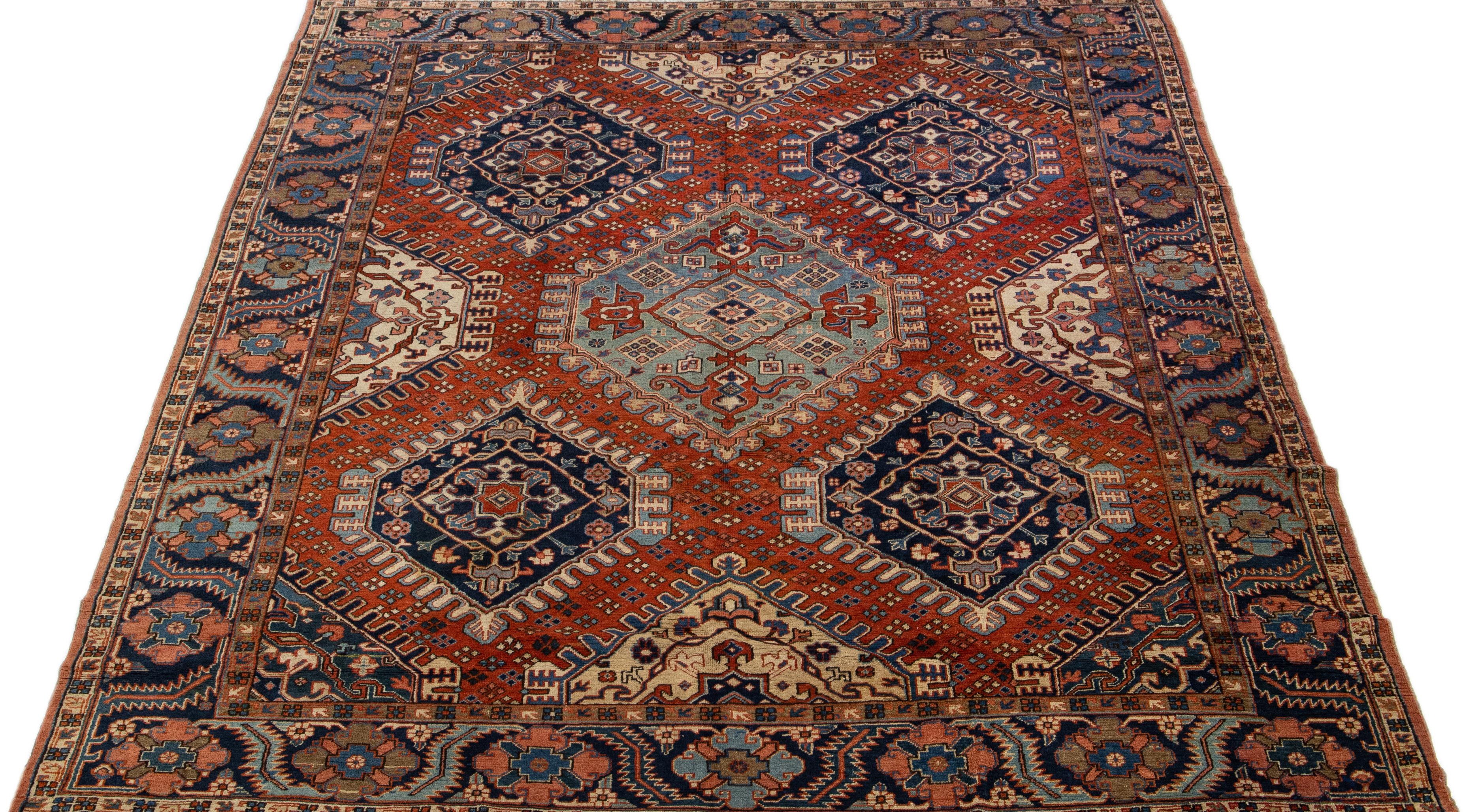 Beautiful antique Heriz hand-knotted wool rug with an orange rust color field. This Persian rug has a navy-blue designed frame and multicolor accents in a gorgeous geometric medallion design.

This rug measures: 10'3