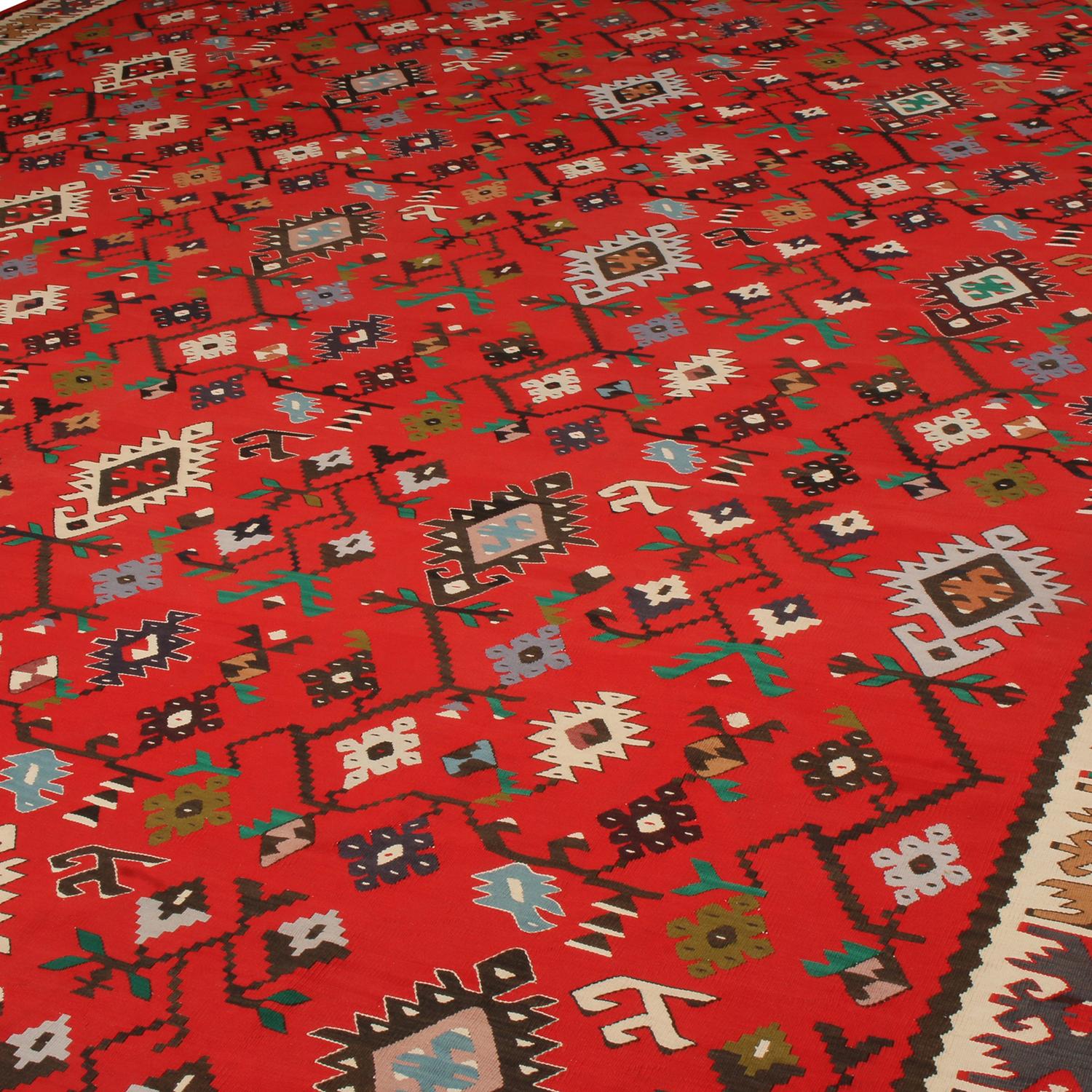 More than 80 years old originating from Turkey, between 1920-1930, this antique Kilim rug hosts an exquisite, balanced medley of spectral and pastel colorways with its rich red background. Flat-woven in high-quality wool with naturally dyed yarn in