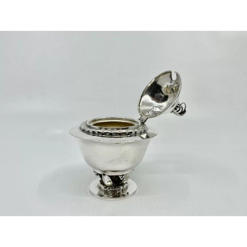 An antique Georg Jensen silver mustard pot, design #236 by Georg Jensen from circa 1917. Mustard pot stands on a stem of four leaves, an acorn is hidden underneath. Rope edge to the foot and upper body and topped with a floral finial.

Additional