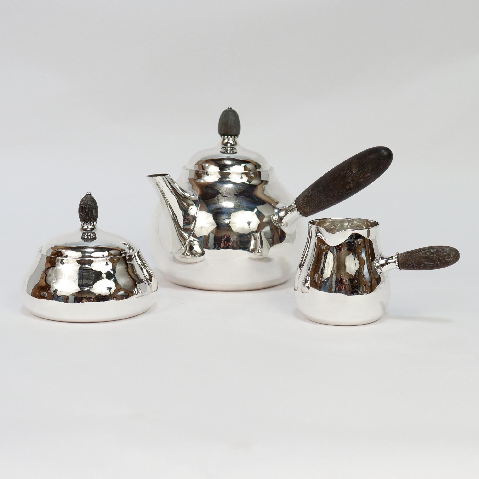 Ein feines signiertes dänisches modernes Teeservice aus Silber.

Von Georg Jensen.

Aus Sterlingsilber.

Muster Nr. 80A.

Bestehend aus einer Teekanne, einer überdachten Zuckerdose und einer Sahnekanne. Jeweils mit Holzgriffen und