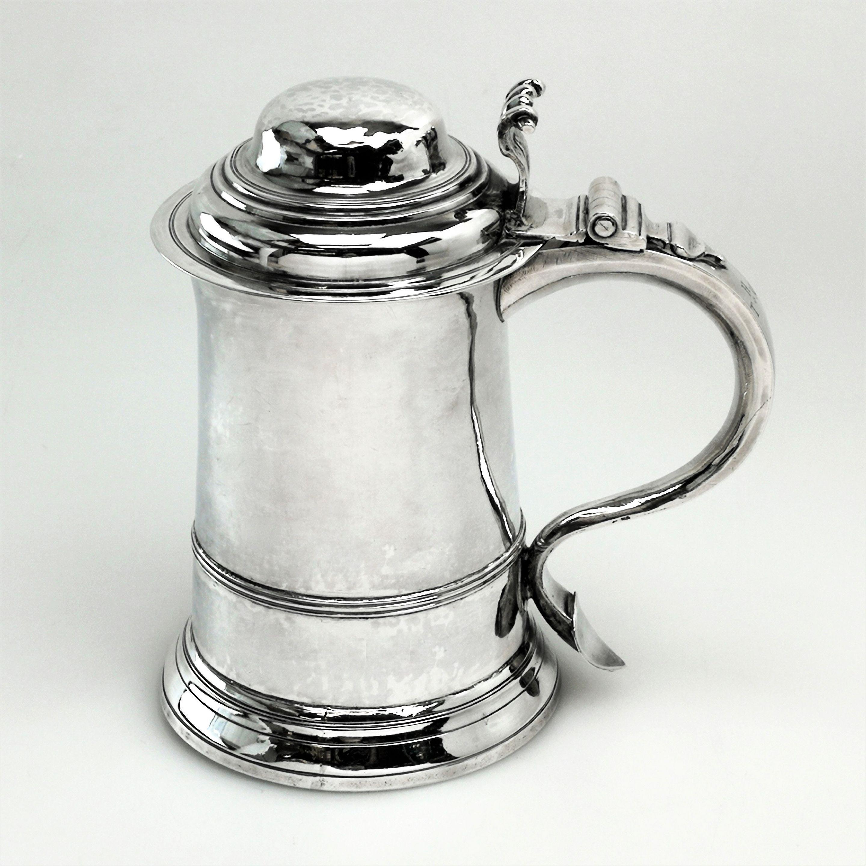 A Classic antique George II Georgian solid silver Tankard in a traditional straight sided design tapering towards a substantial domed lid. The Tankard has a large scroll handle and a scroll shaped thumb piece. There are three initials engraved on