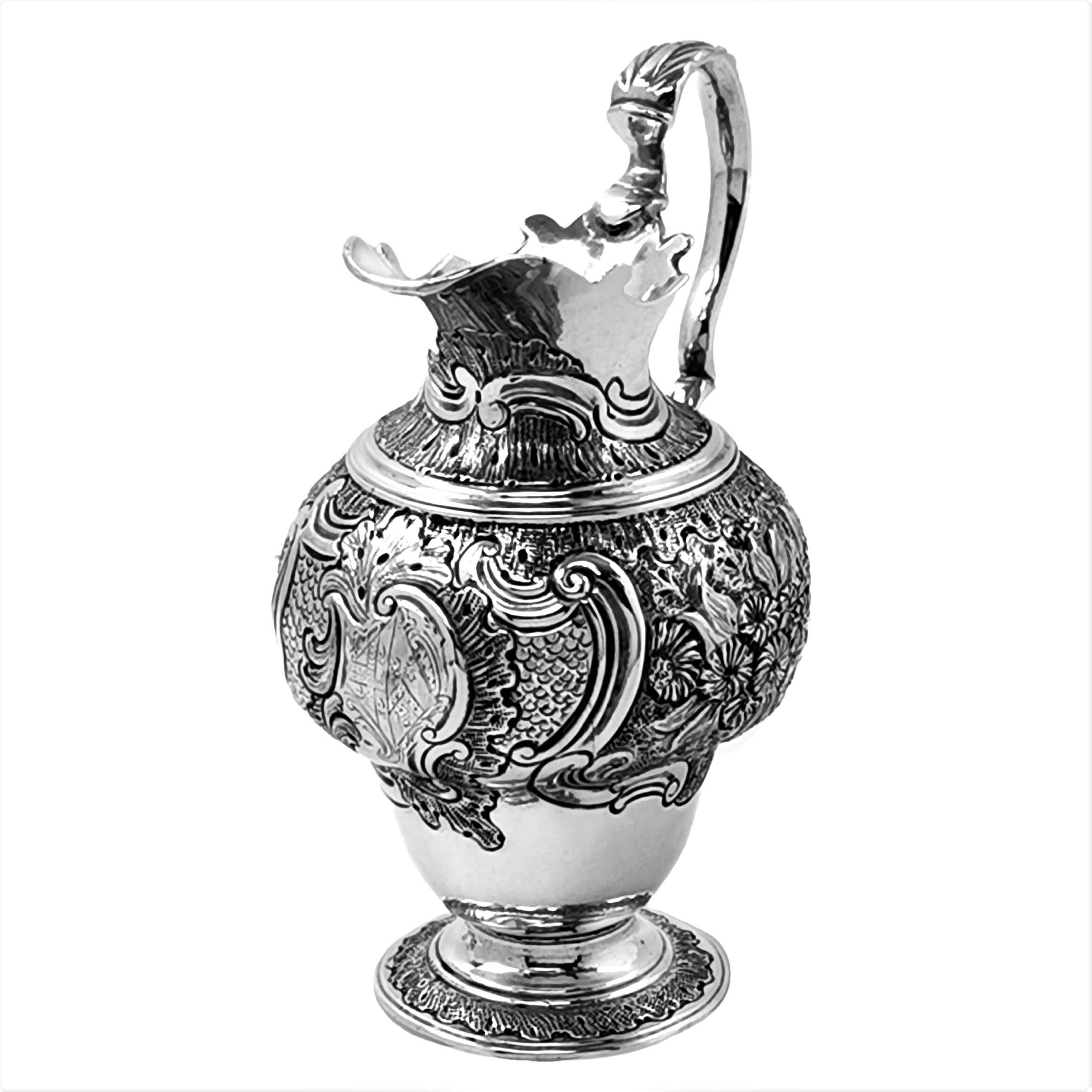 A lovely Antique George II sterling Silver Cream Jug with an ornate floral chased design. The Cream Jug has a engraved armorial in a central cartouche. The Jug stands on a chased spread foot.

Made in London, England in circa 1750 by John