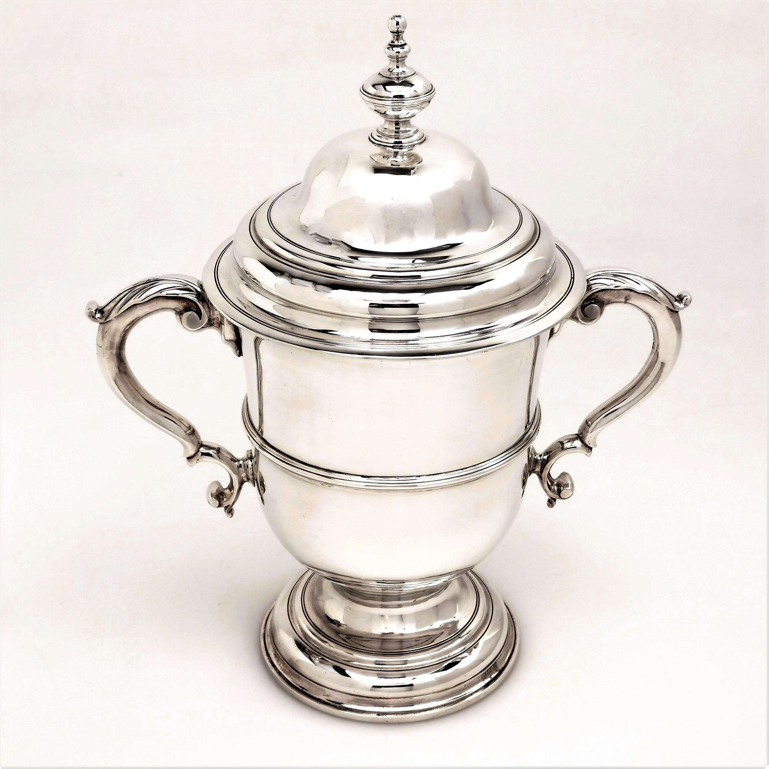 A beautiful antique George II two handled cup and cover in a Classic Georgian Style. The cup has two impressive acanthus leaf topped scroll handles and stands on a spread pedestal foot. The body of the trophy has a central band and a large armorial