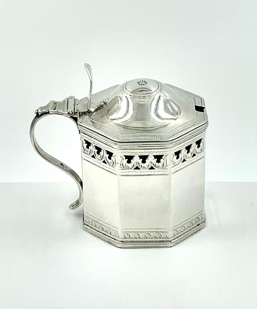 Superb Armorial, rare octagonal reticulated silver mustard pot by Henry Chawner, 1794. The front panel finely engraved with a heraldic crest of a hand holding the Fleur-de-Lis. 
The top of this mustard pot is fitted with an octagonal domed cover