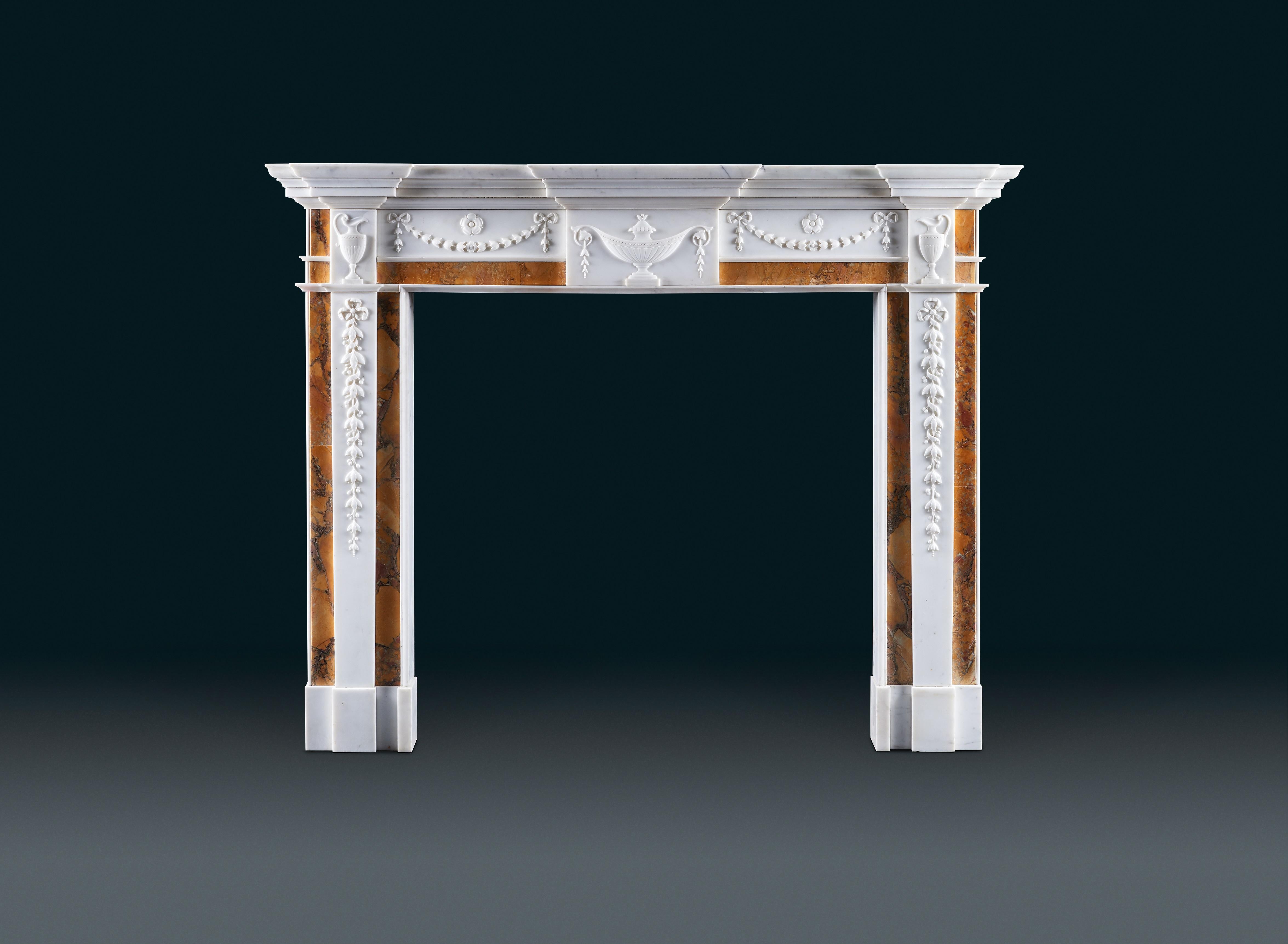 A late George III, Irish neoclassical antique chimneypiece of Siena and statuary marbles. The breakfront moulded shelf above the frieze which is decorated with a central tablet carved with a lidded tazza urn with scrolling handles, echoed by further