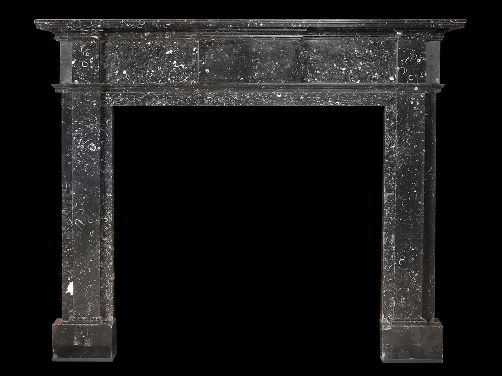 A George III Kilkenny marble fireplace of simple composition, with plain pilaster jambs, centre tablet and end blocks. All beneath a stepped and moulded shelf. The whole raised on square foot blocks, late 18th or turn of the 19th century,