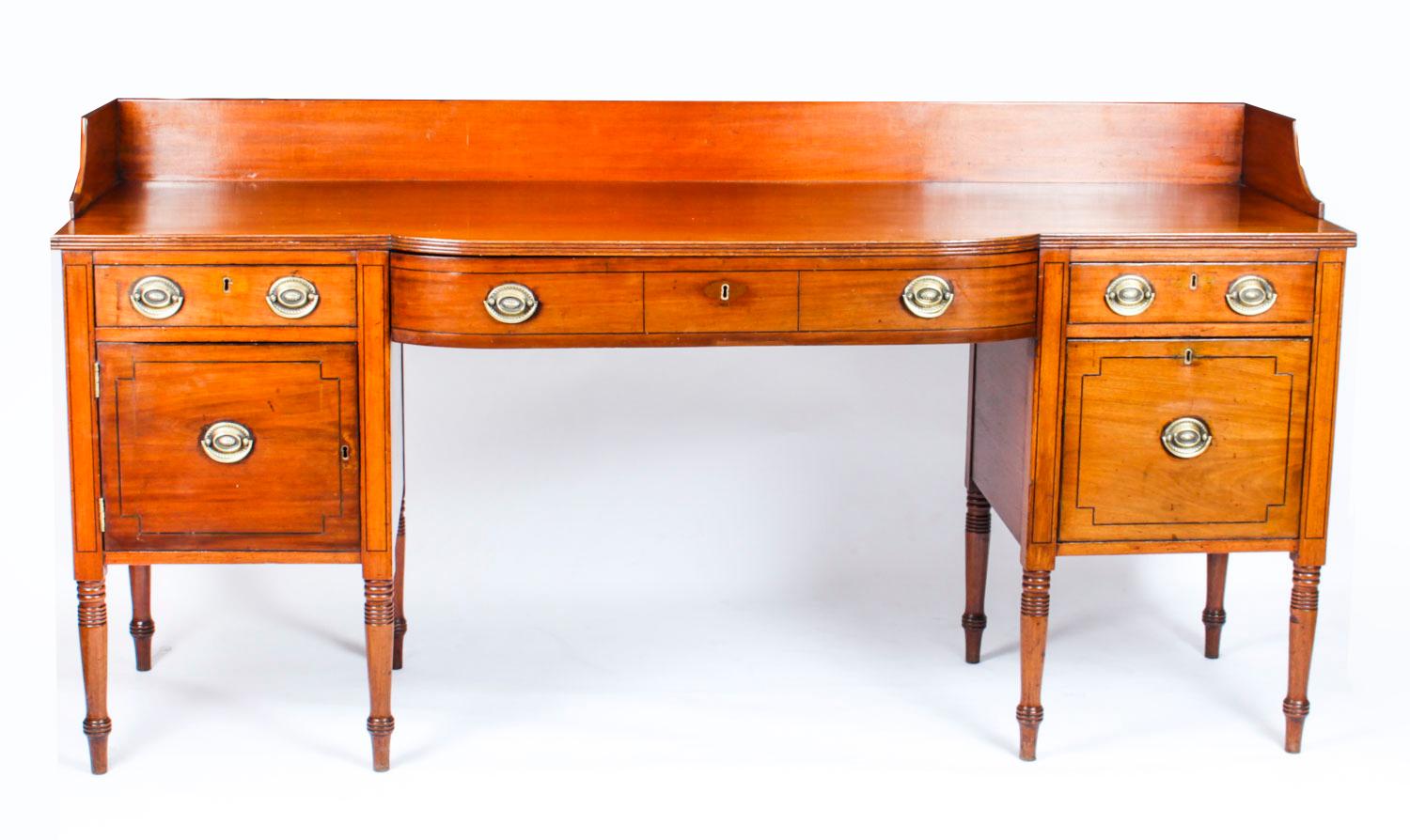 This is a superb antique flame mahogany and ebonized line inlaid bow front George III sideboard, circa 1790 in date.

The splendid shaped stage back is above three frieze drawers above a cupboard on the left with a cellarette drawer on the
