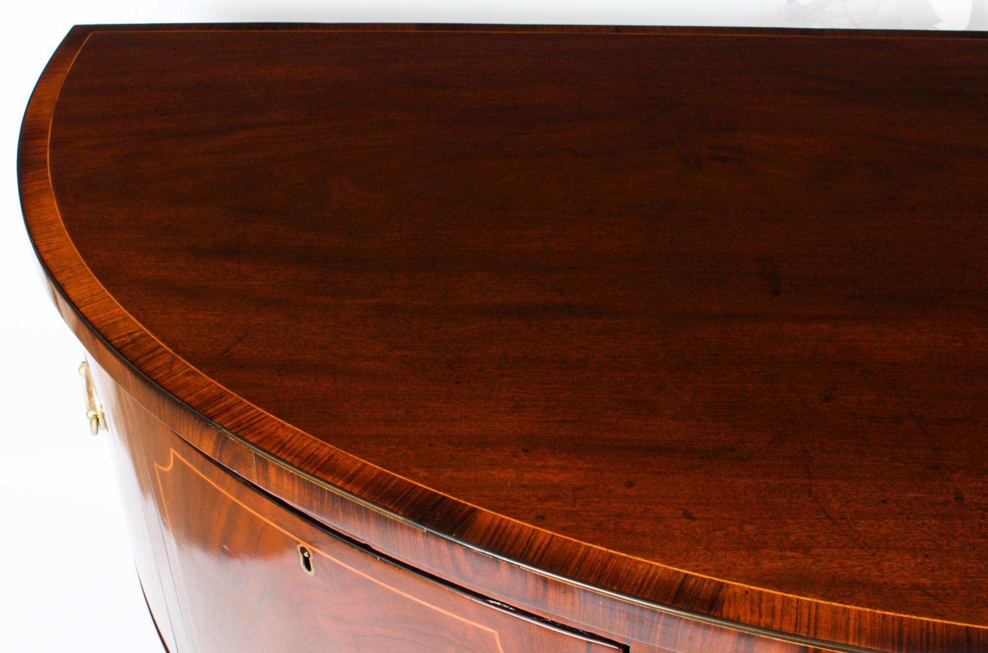 This is a superb antique walnut and satinwood line inlaid bow front George III sideboard, circa 1790 in date.
 
The splendid demi-lune shaped sideboard features satinwood inlaid stringing with shell inays with three frieze drawers above a cupboard