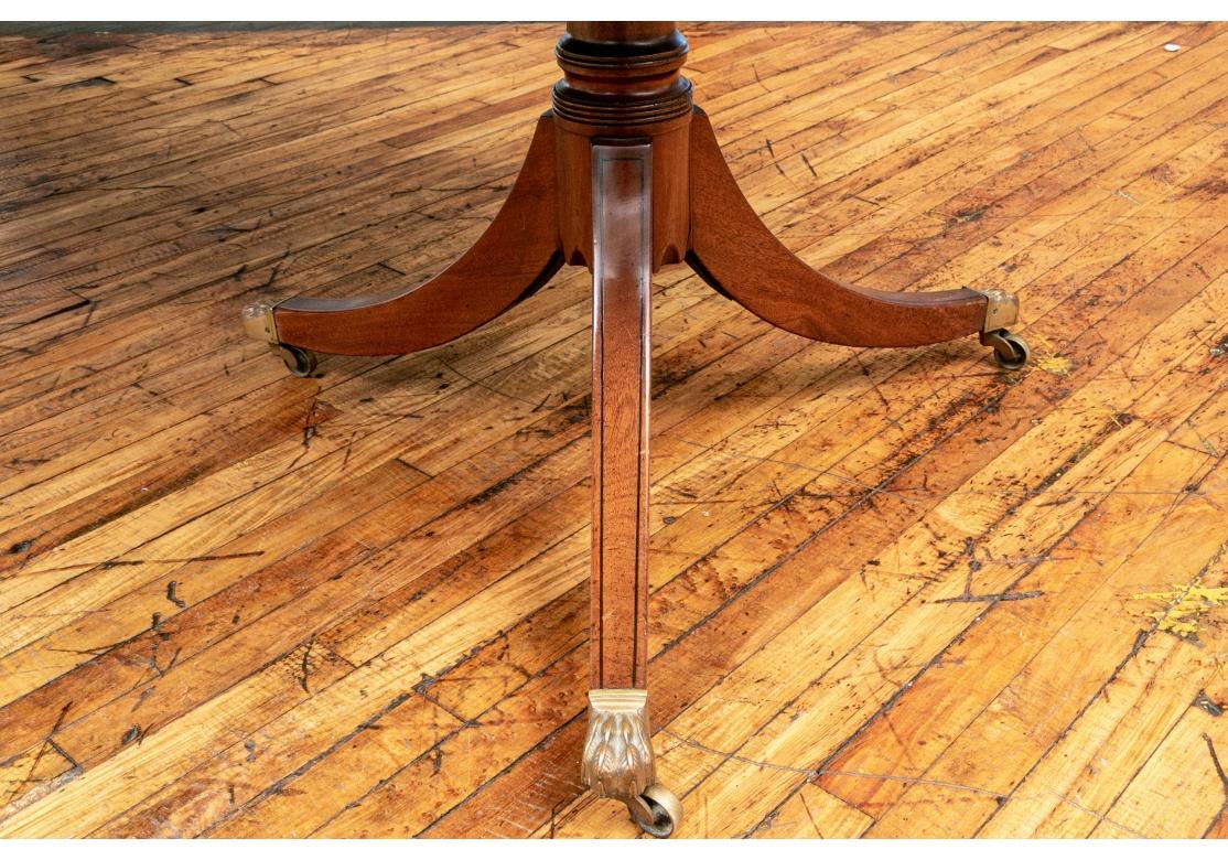 Fina mesa de comedor de caoba con dos hojas. Extremos superiores redondeados con borde estriado. Los pedestales dobles están tallados y torneados con extremos curvos dentados. Las patas están unidas con incrustaciones de cuerda ebonizada y finas