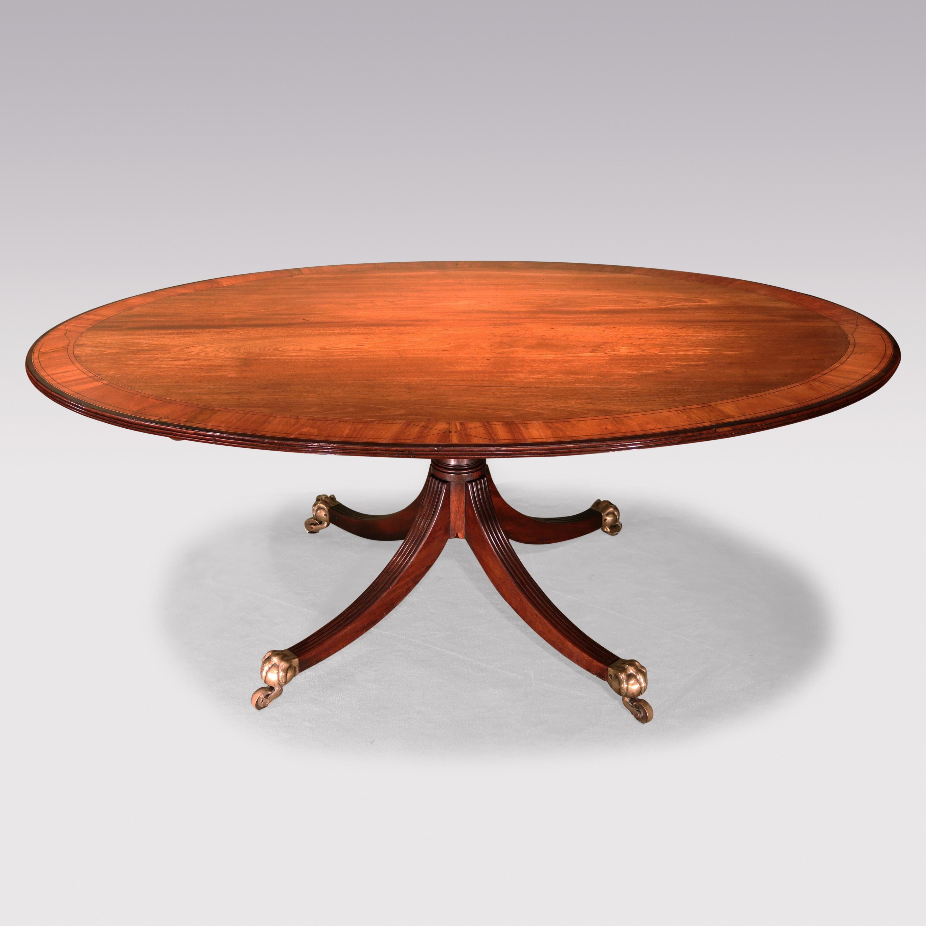 A fine and large George III period figured mahogany Breakfast Table, having boxwood & ebony strung & satinwood & purpleheart crossbanded reeded edged oval top, supported on gun-barrel stem ending on reeded 4-splay legs retaining original brass paw &