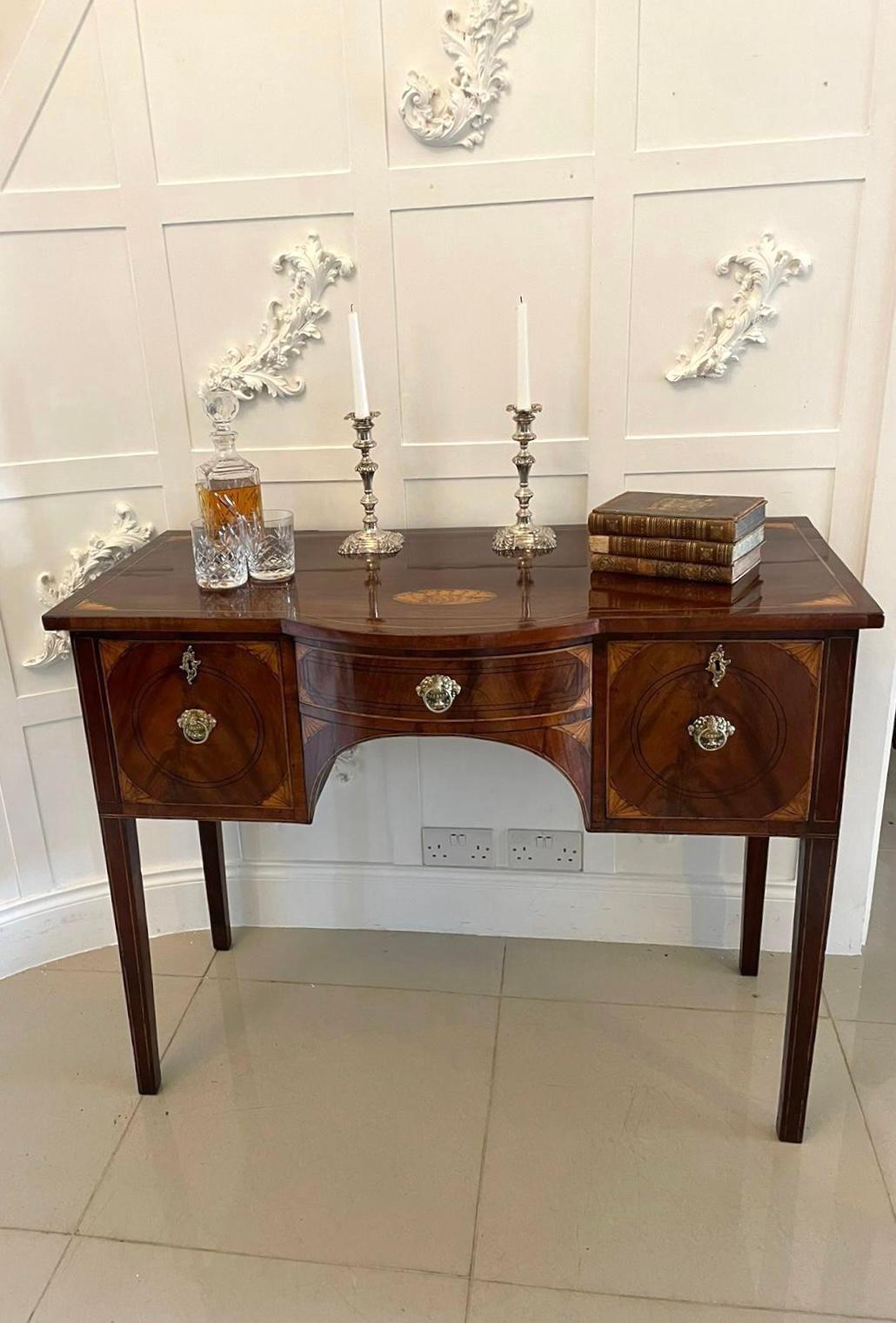 Antique George III quality mahogany inlaid sideboard having a quality mahogany top inlaid with pretty satinwood shells, boating a bow fronted drawer to the centre flanked by one drawer and a cupboard door with ornate brass handles in figured