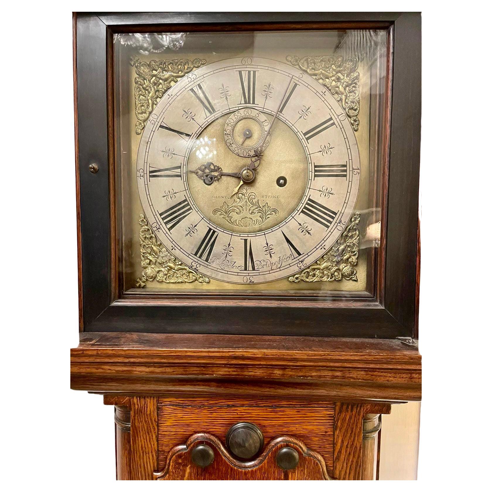 Date 1720 Antique George III quality oak longcase clock by Jacob Lovelace, Exeter having a removable hood with a shaped cornice pierced carved frieze glazed door flanked by two turned columns, long shaped door with unusual pierced carved centre